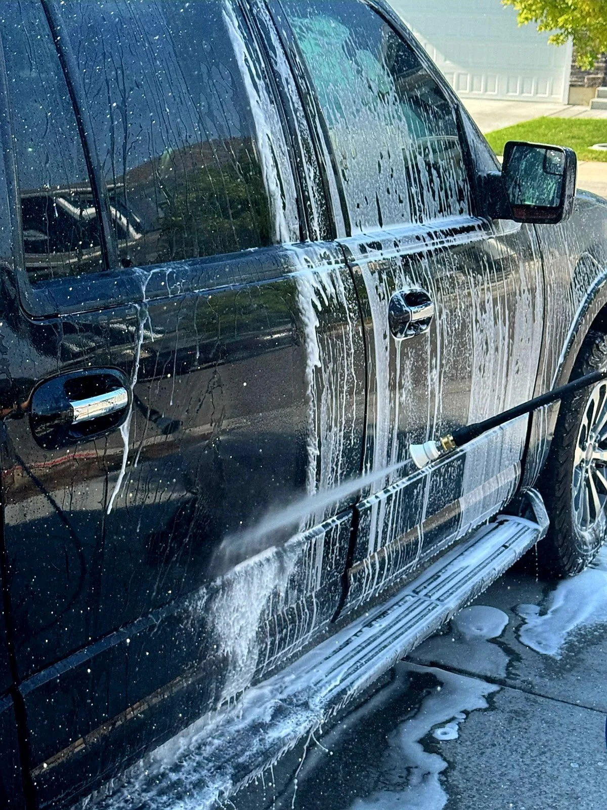 A black pickup truck being washed with soap and a hose outside a house.