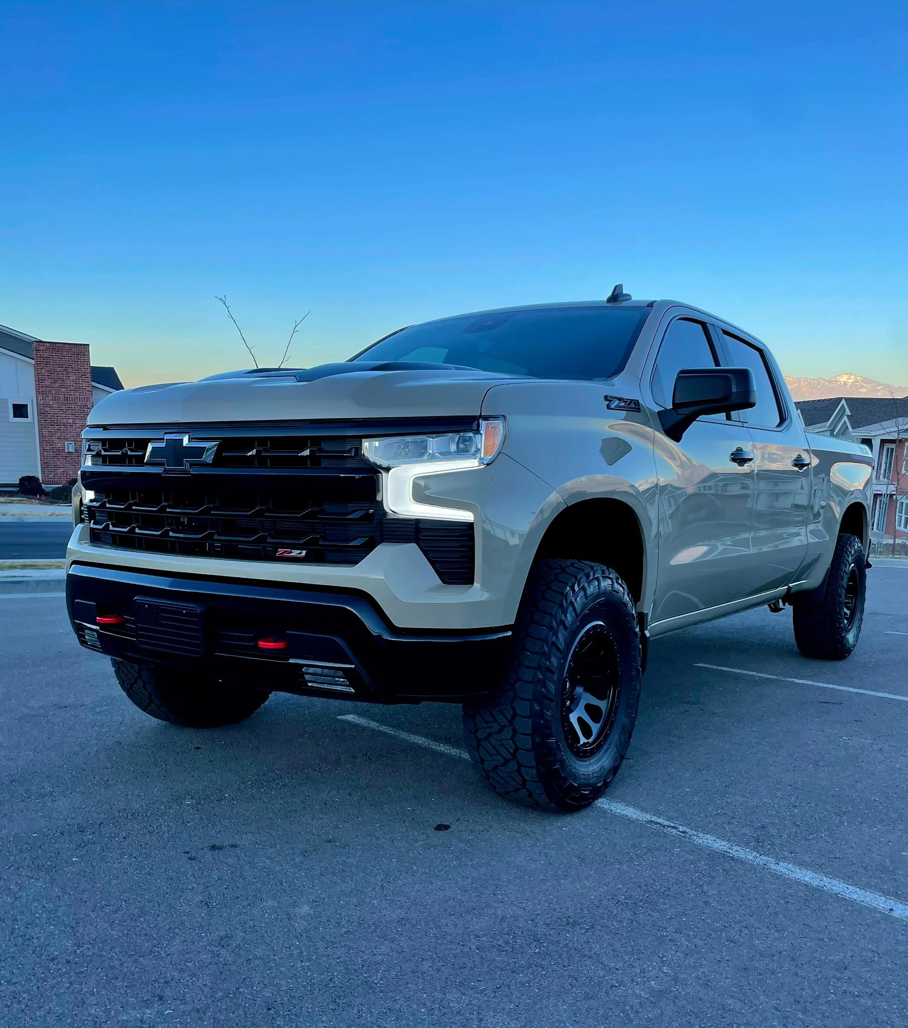 A white Chevrolet pickup truck with off-road tires parked in a parking lot during sunset.