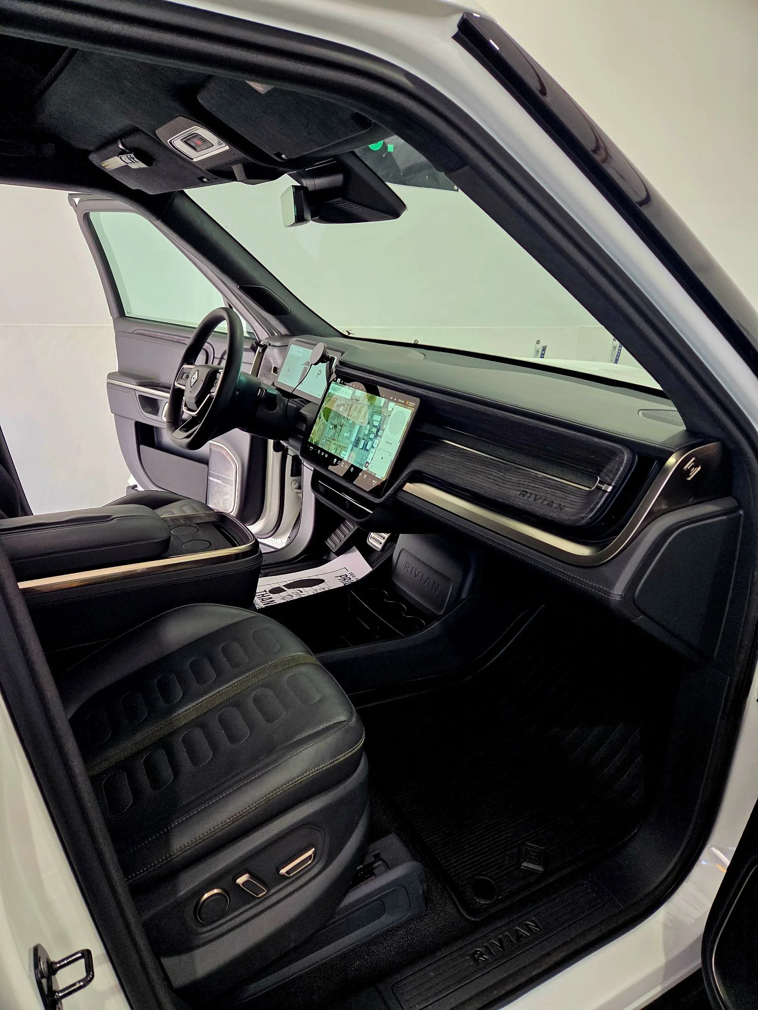 Inside view of a modern vehicle interior with digital displays on the dashboard, a black leather seat, and a door open revealing part of the exterior.