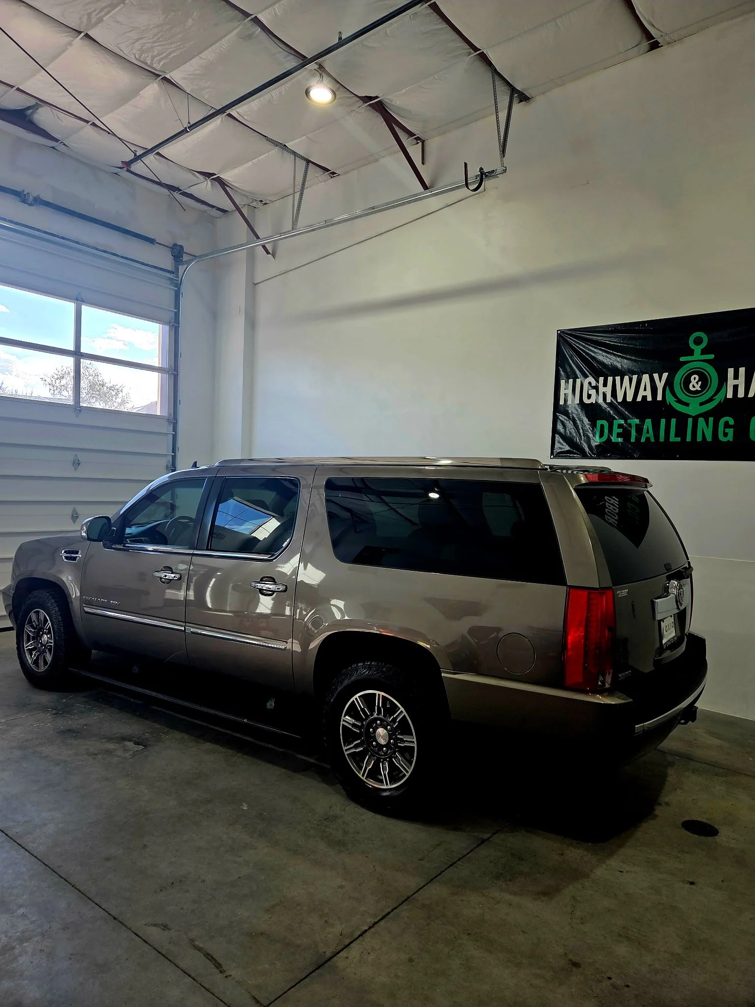 A parked gold-colored Cadillac SUV inside a garage with a large window and a high ceiling.