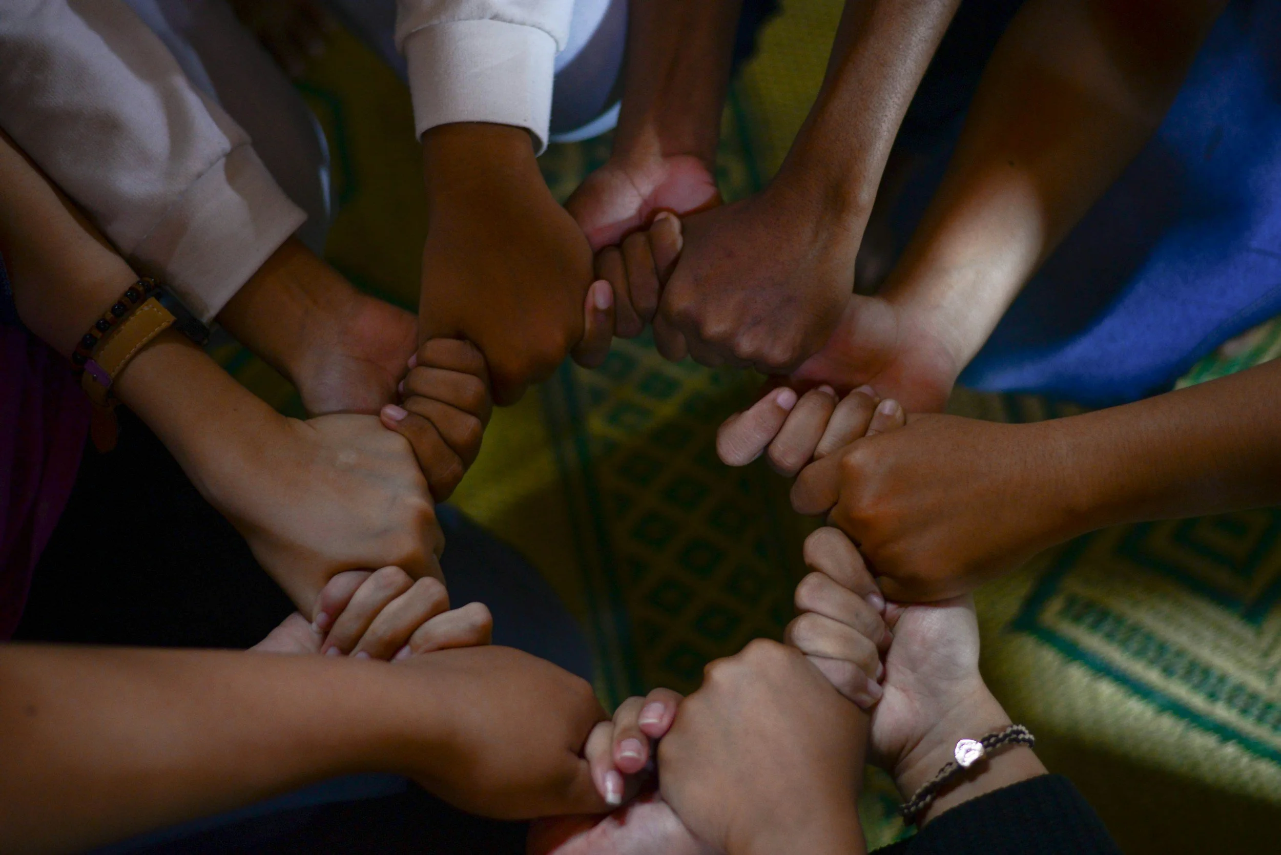 Multiple hands of diverse skin tones joined together, forming a heart shape.