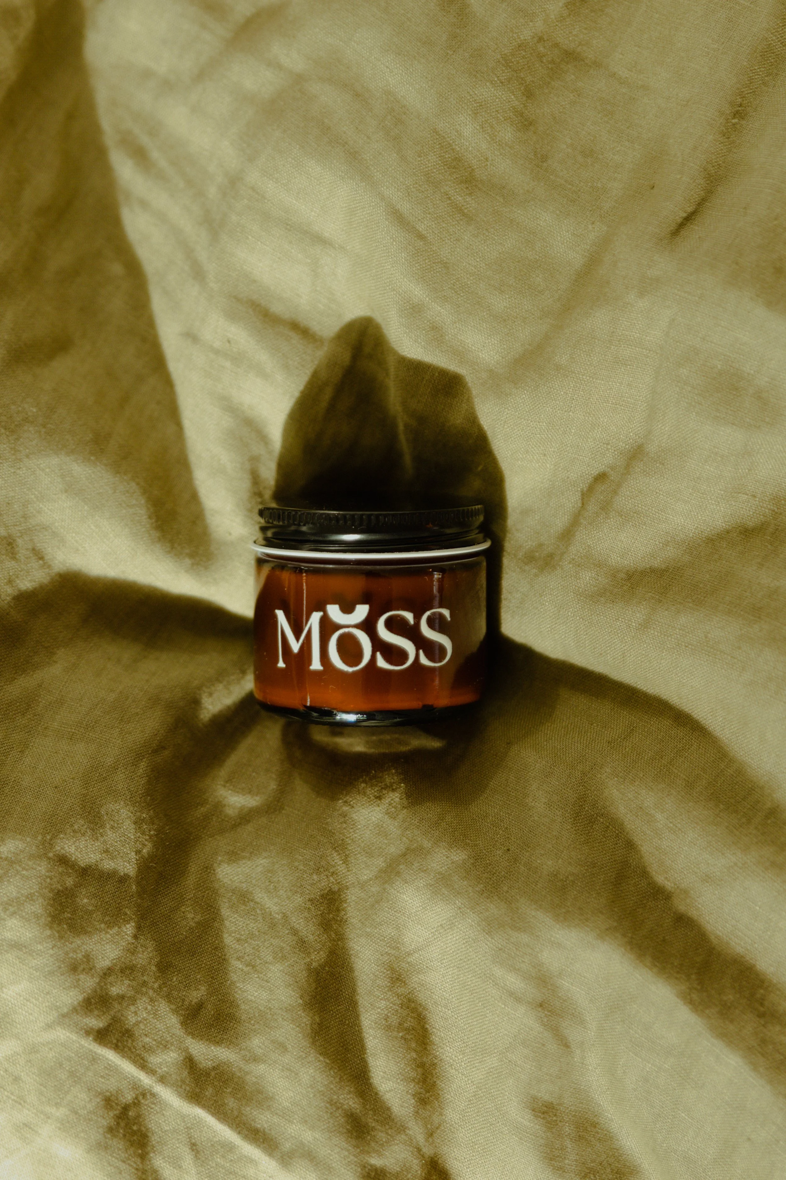 An amber jar of Moss Gabriola's vegan moisturizer for dry Canadian winterslaying on a taupe sheet.