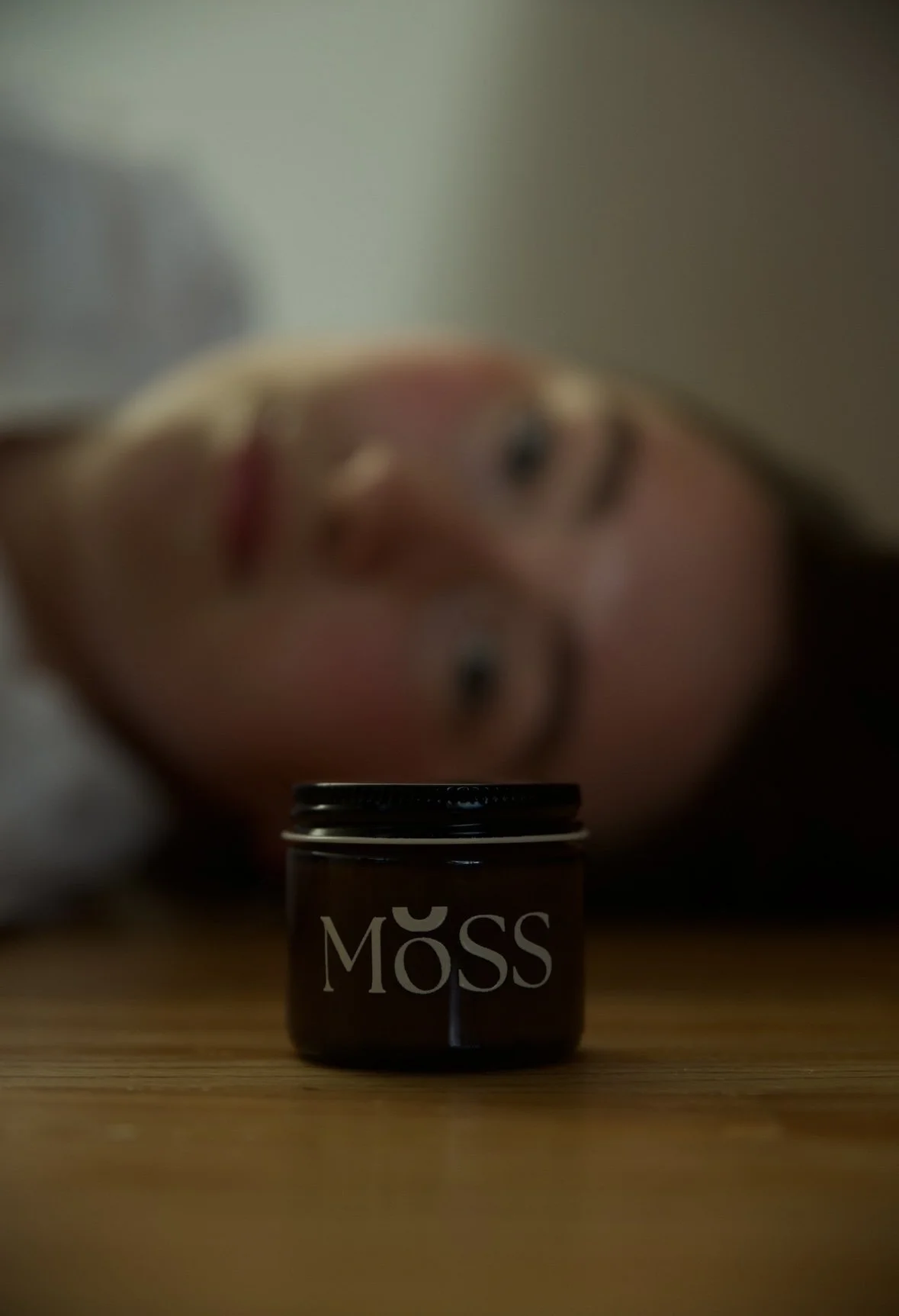 Blured face of a women laying down behind an amber glass jar of Moss Gabriola's natural moisturizer in Canada. Learn more about organic skincare.