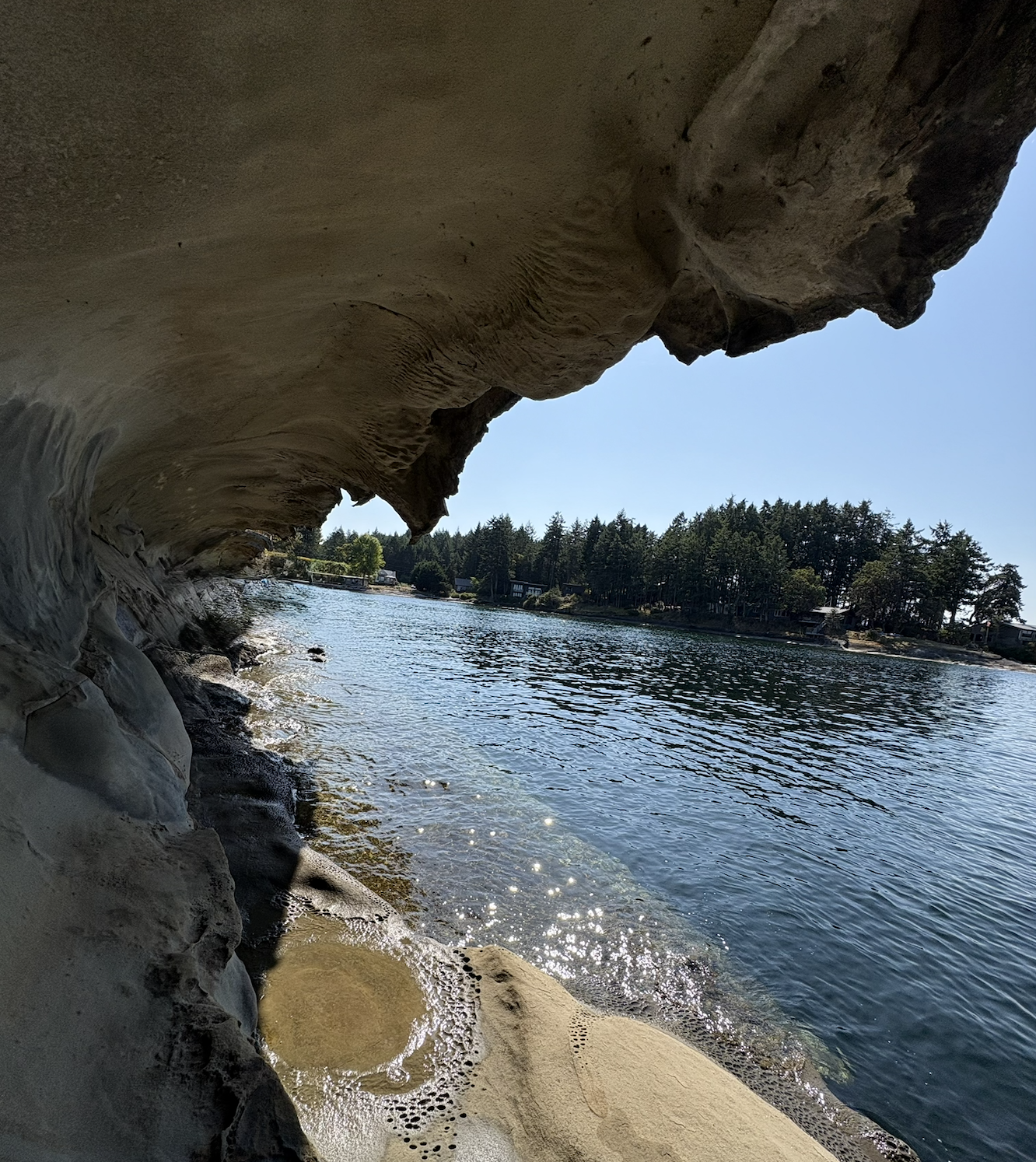 View of a rocky overhang by a river with trees and houses on the opposite bank