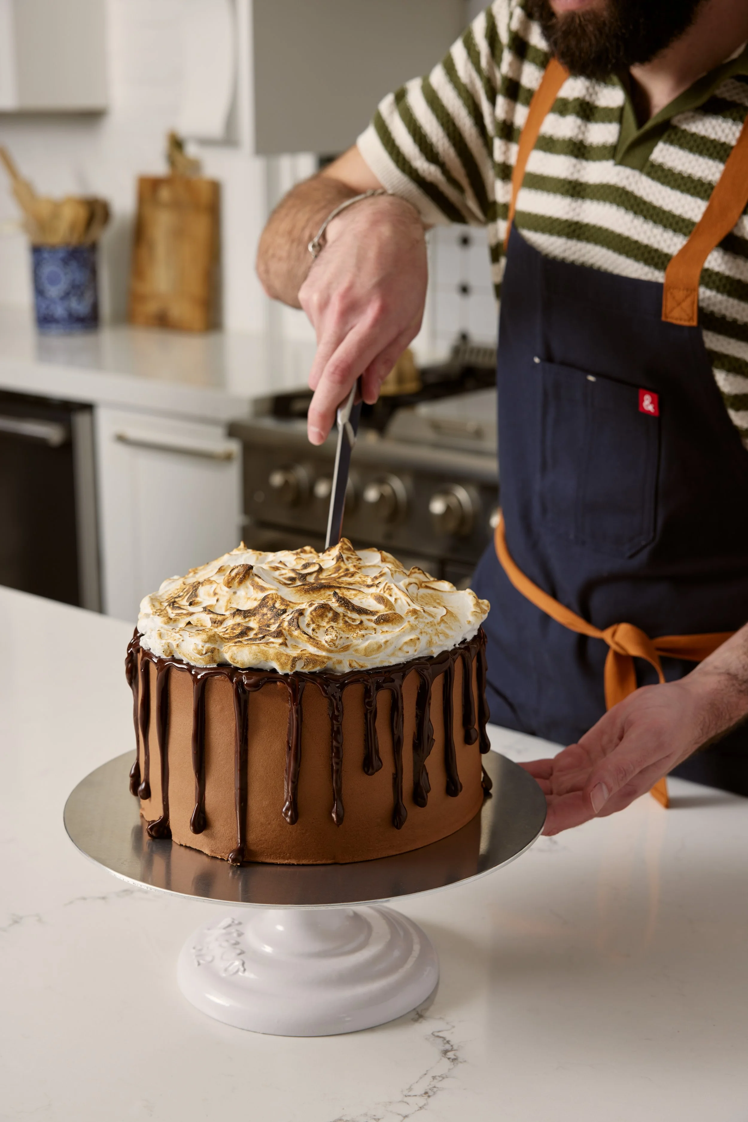 Close-up of a man decorating a chocolate cake with toasted meringue on top in a kitchen.