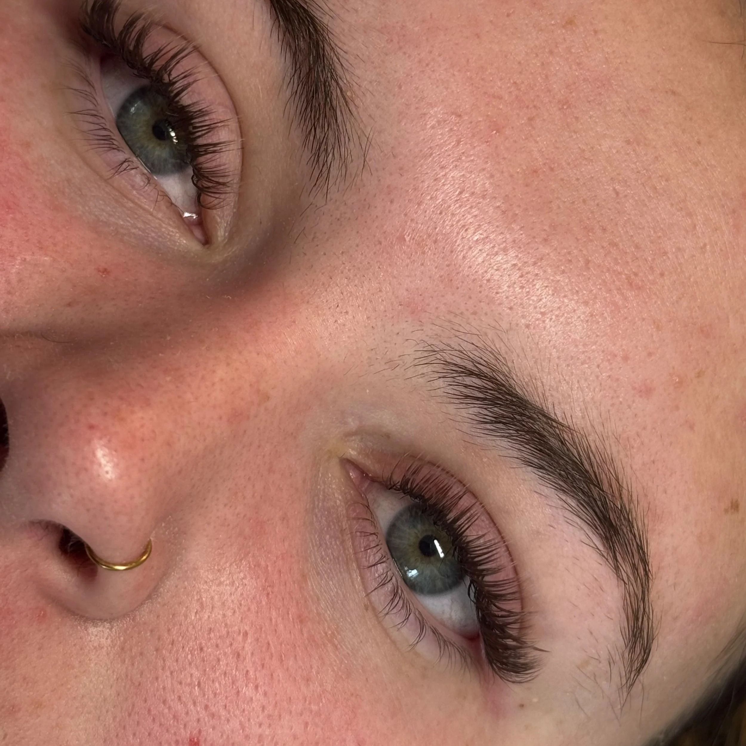 Close-up of a woman's face, focusing on her eyes and eyebrows, with natural skin and a nose ring.