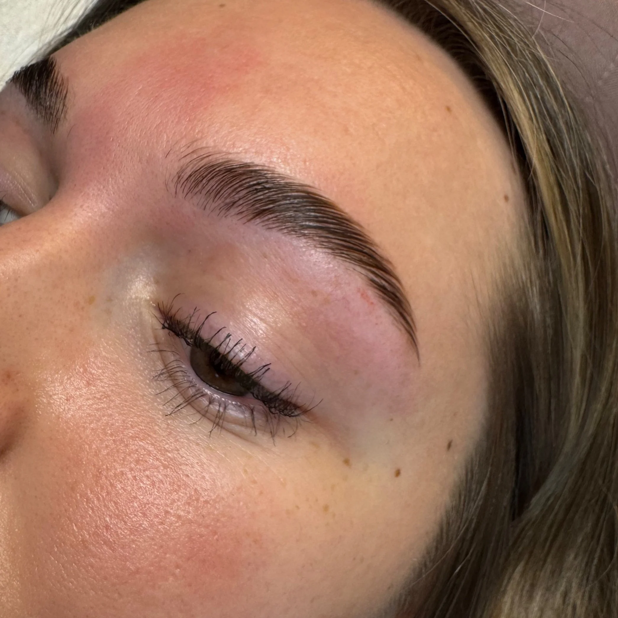 Close-up of a woman's face showing her eye, eyebrow, and part of her forehead with natural skin texture and freckles.