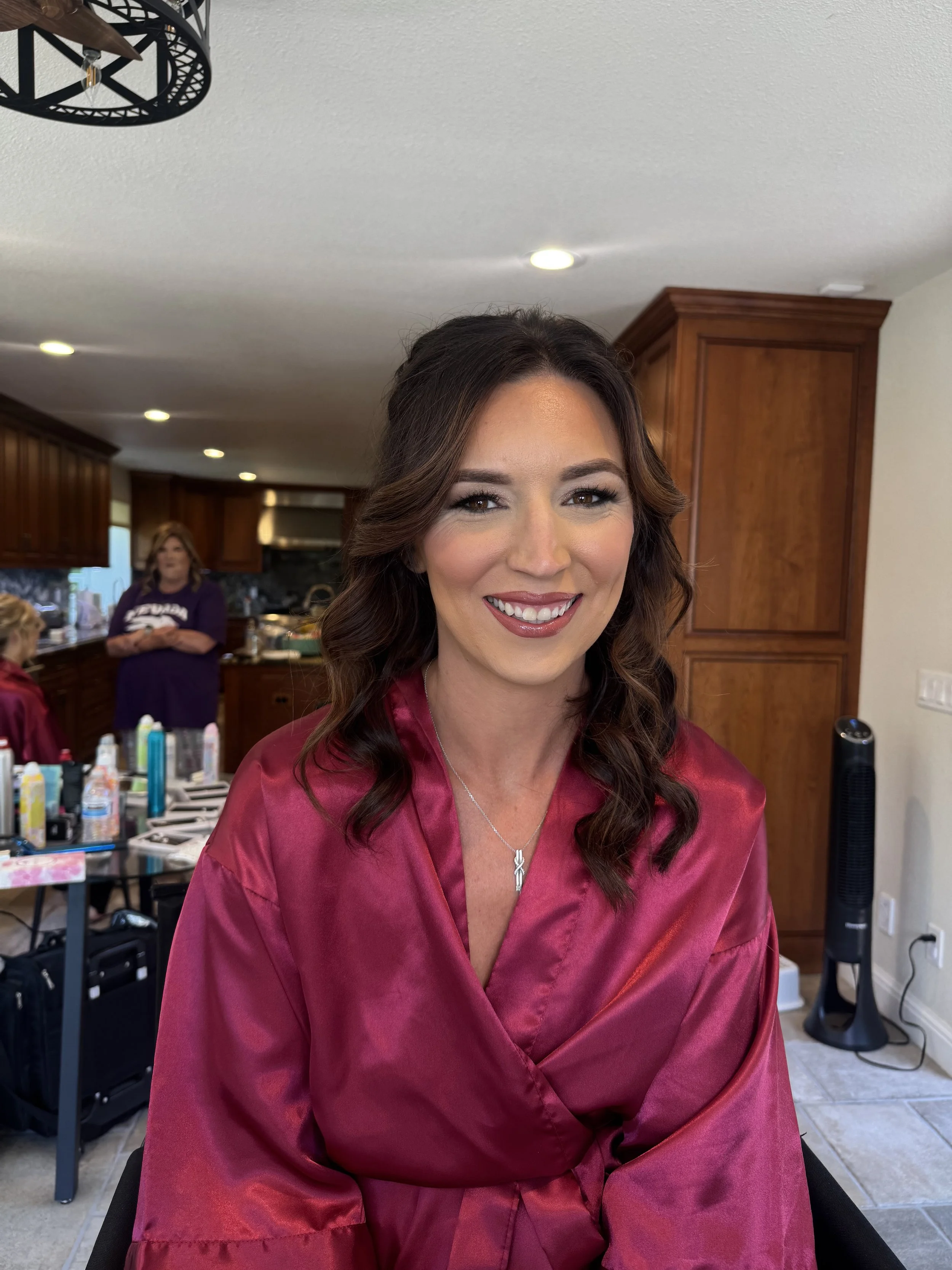 A woman with brown hair wearing a maroon satin robe, smiling, in a kitchen with wooden cabinets.