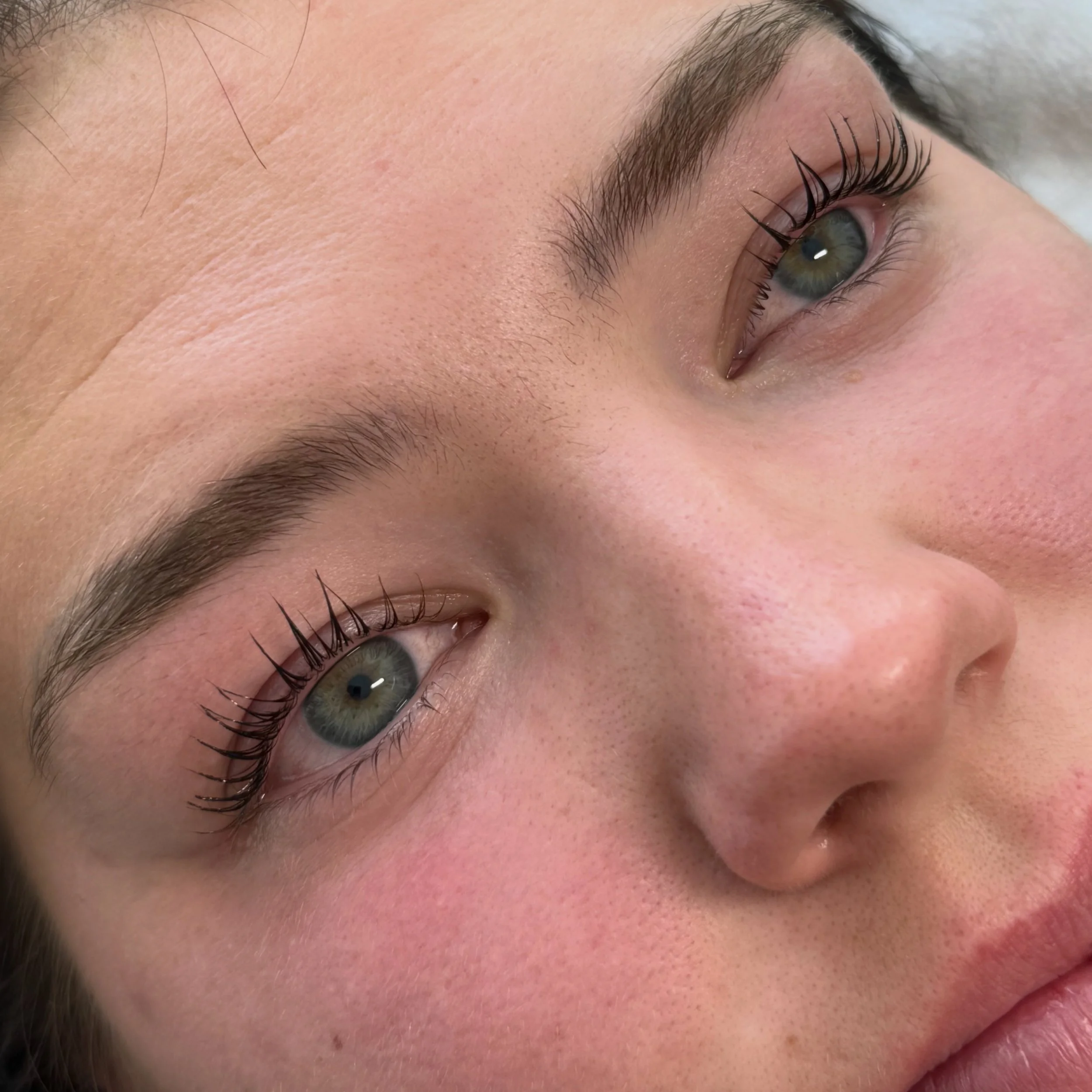 Close-up of a person's eye with long eyelashes and well-groomed eyebrows, showing skin with natural texture and freckles.