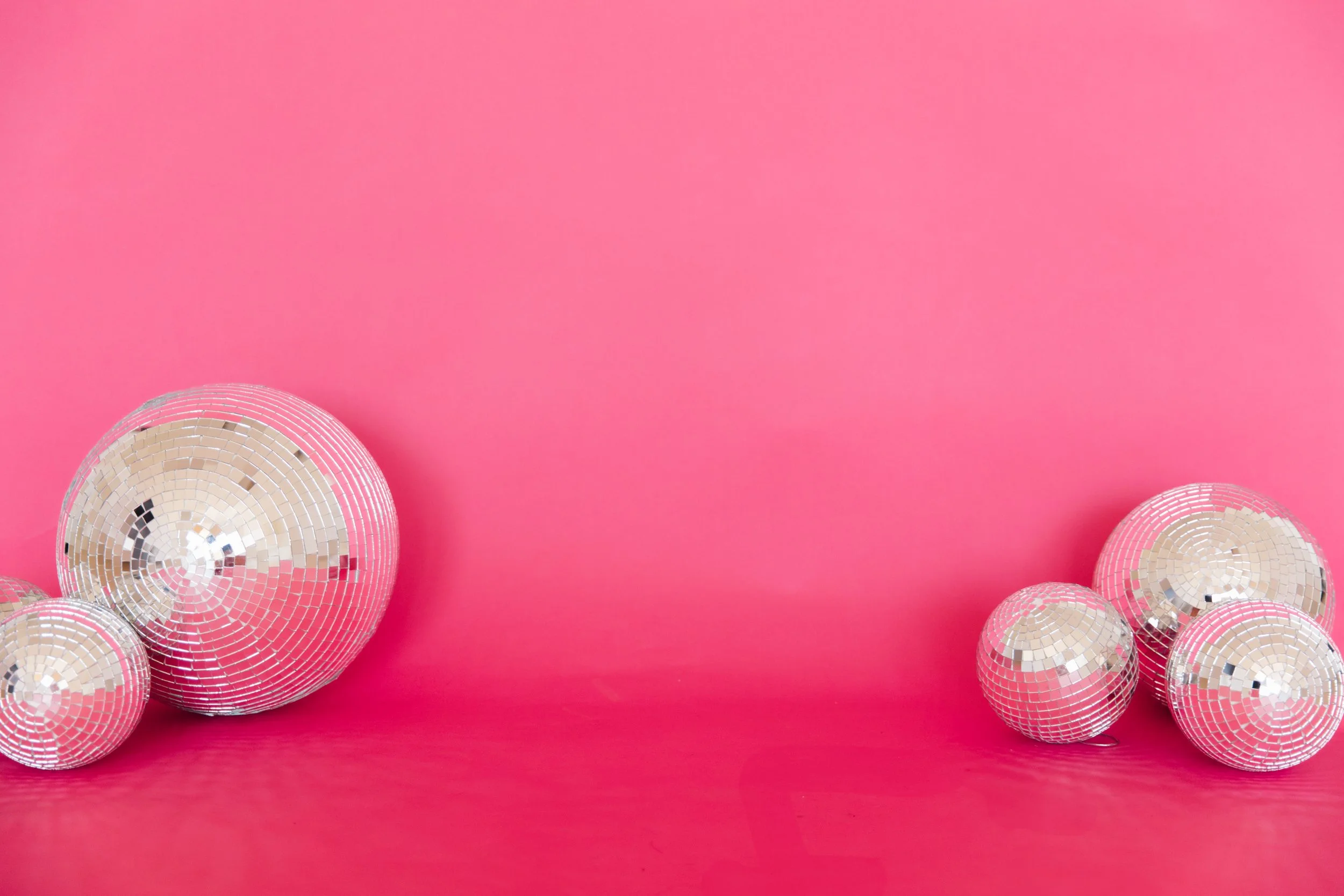Multiple disco balls placed on a bright pink background.