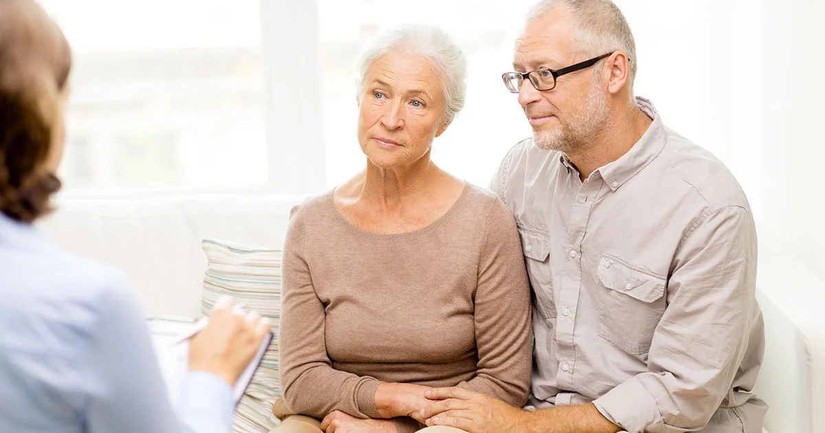 An elderly woman and a middle-aged man sitting together during a medical appointment, talking to a healthcare professional.