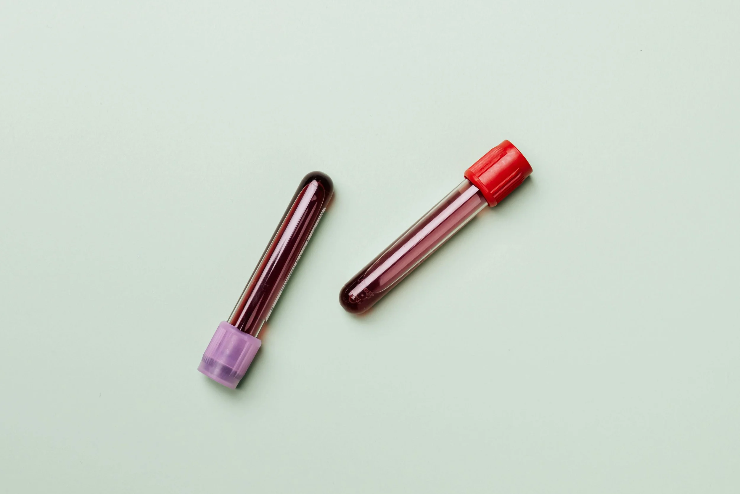 Two blood sample vials with purple and red caps on a light green background.