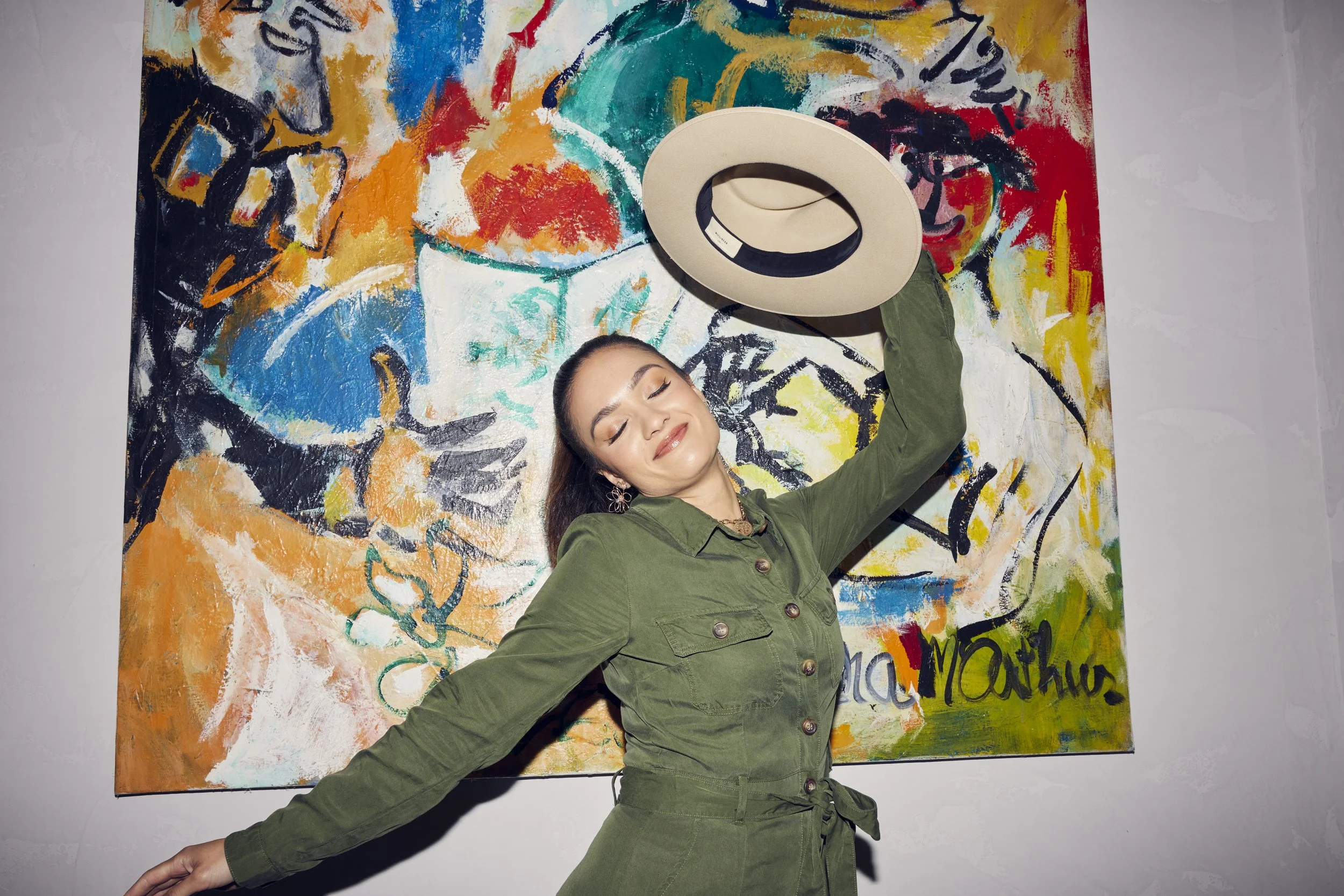 Happy traveller holding a hat in front of a painting
