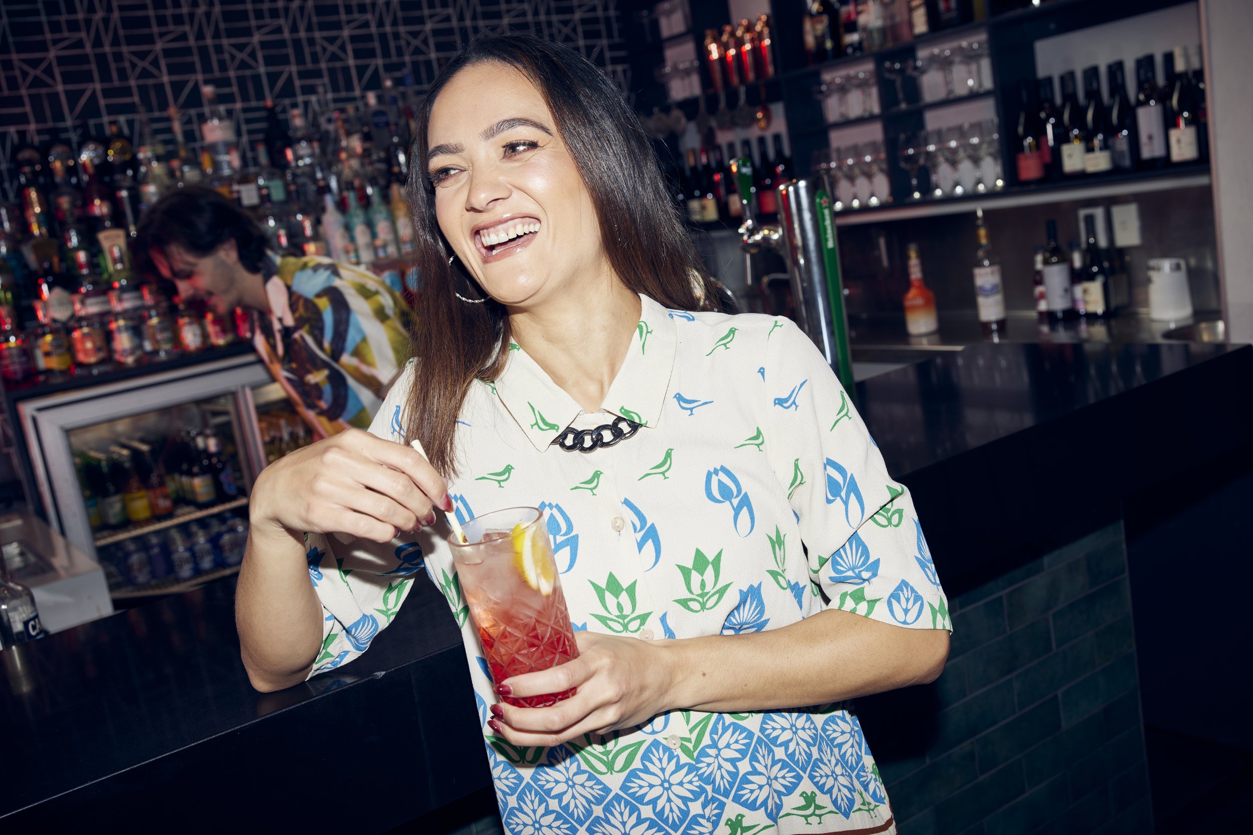 Woman enjoying a red cocktail at a modern bar with a relaxed, social atmosphere.