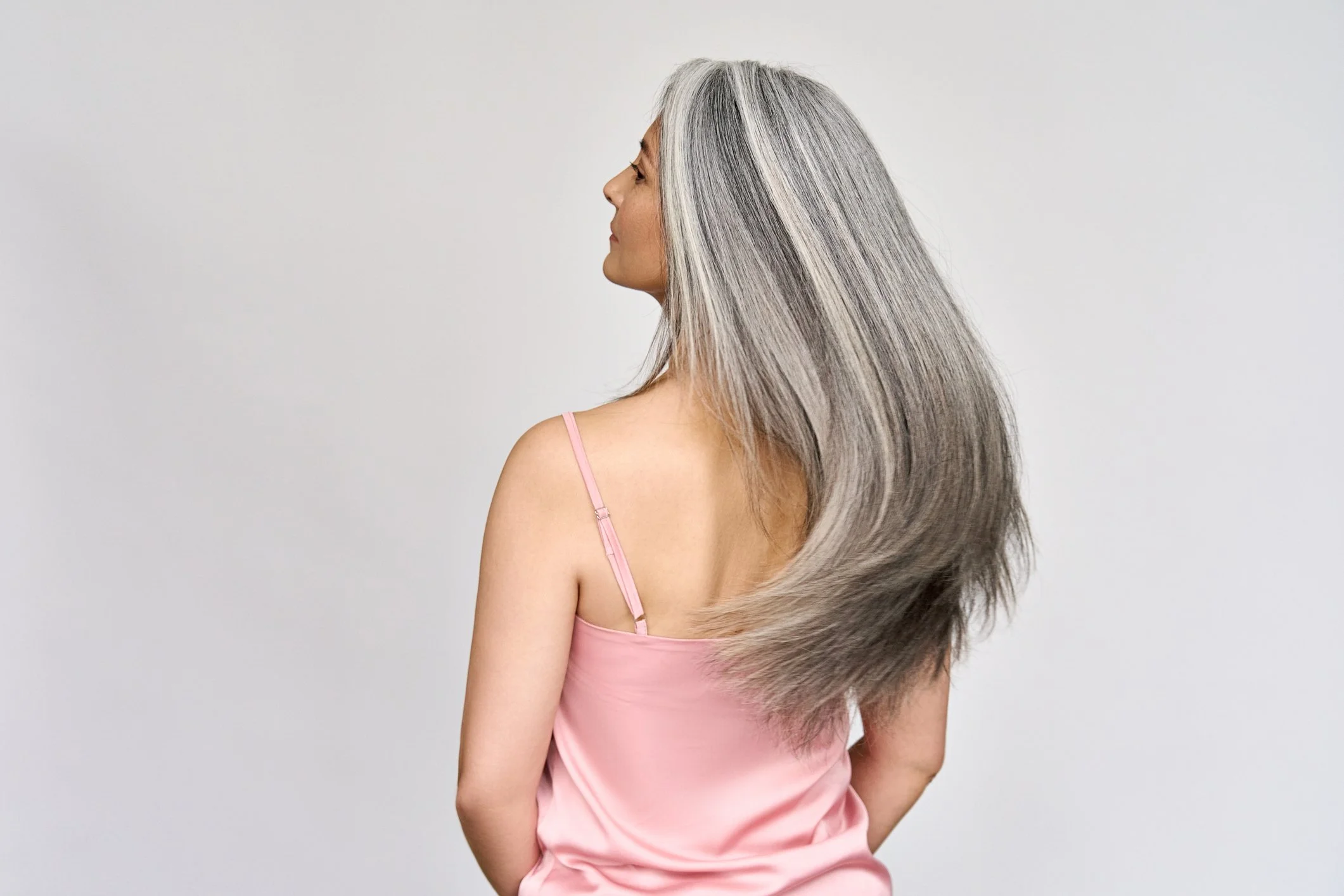 A woman with long gray hair in a pink slip looking to the side against a plain light gray background.
