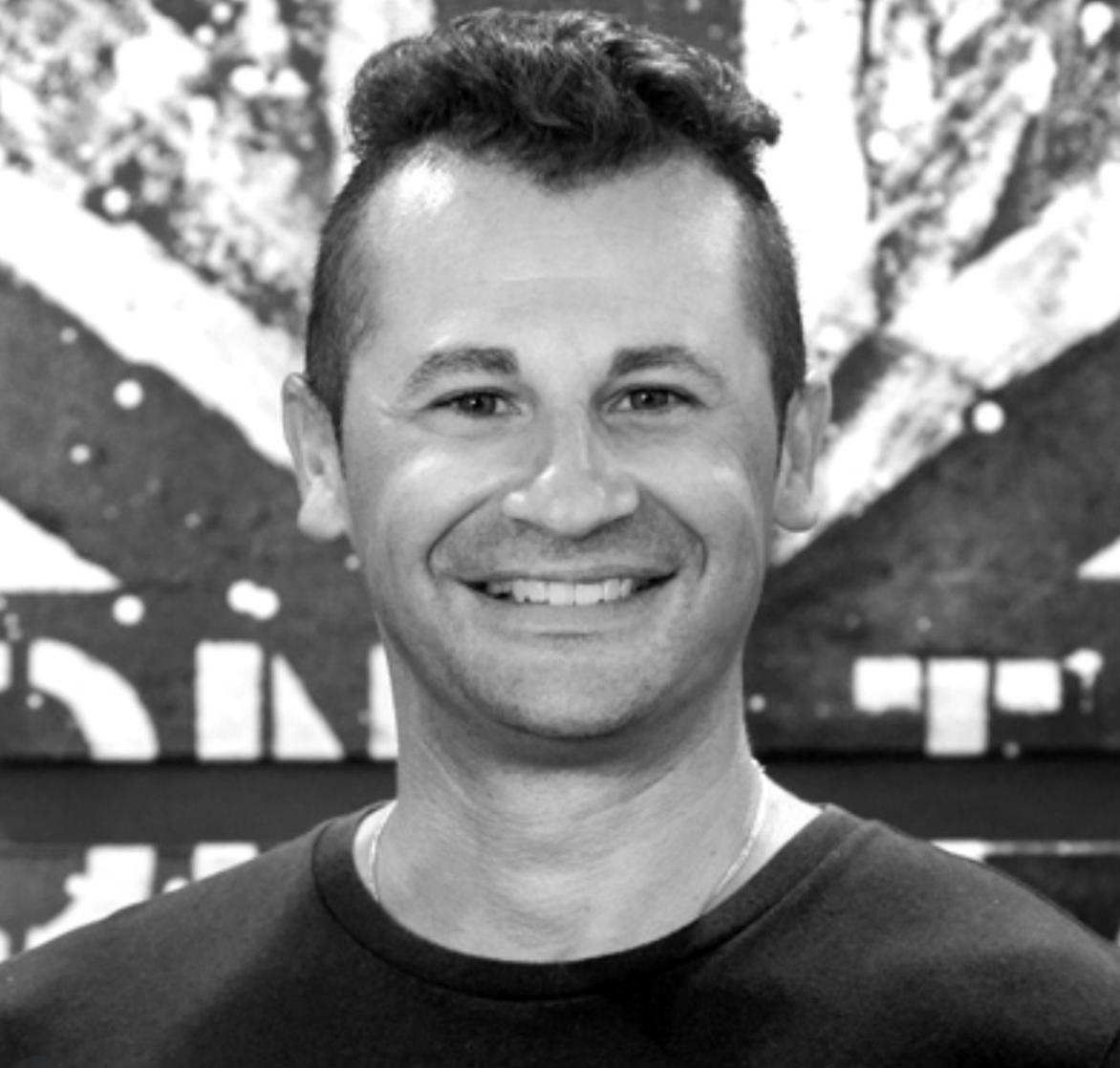 A smiling man with short, dark hair in front of a decorated background.