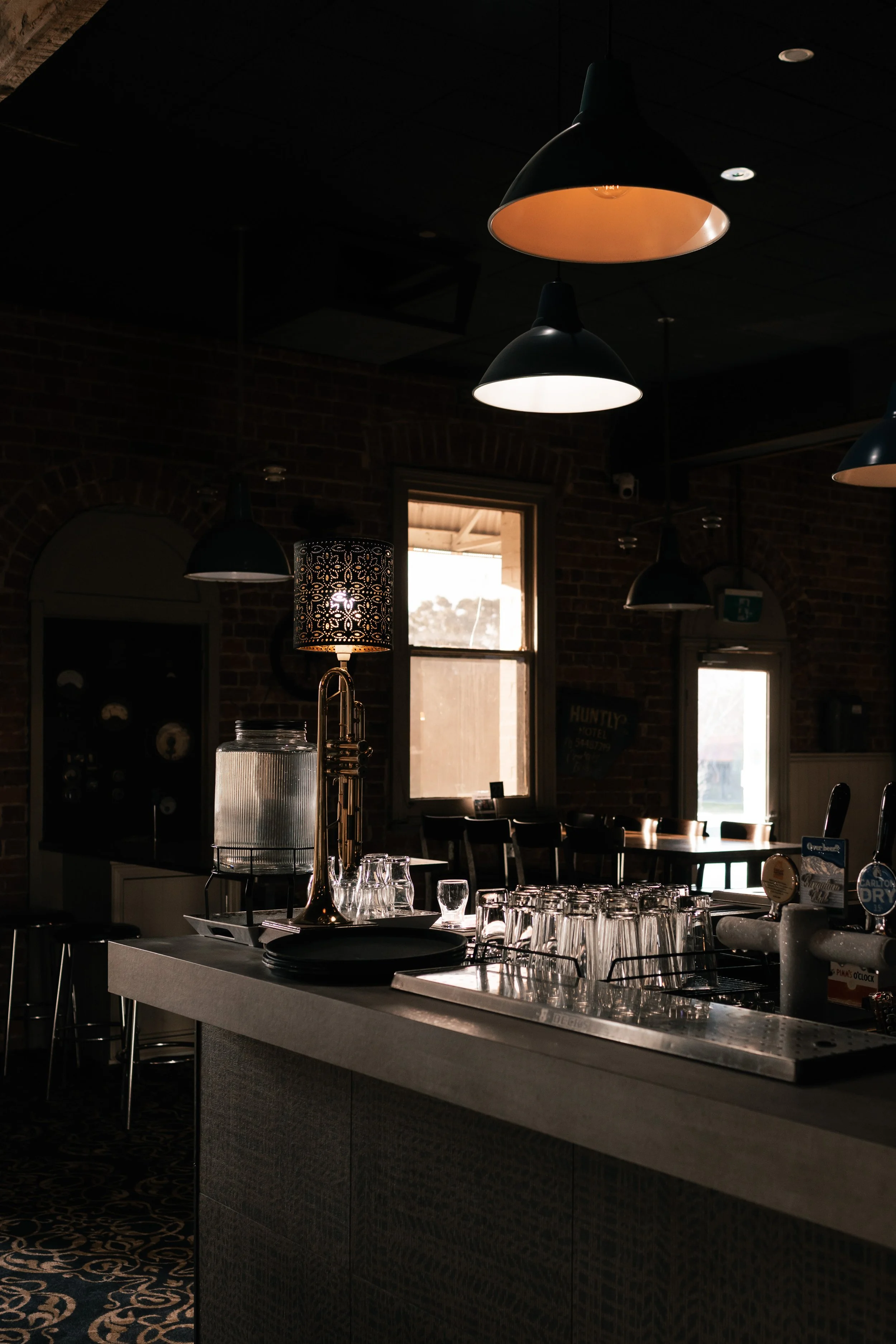 Empty bar with glasses, water pitcher, and a lamp, inside a dimly lit restaurant or café.