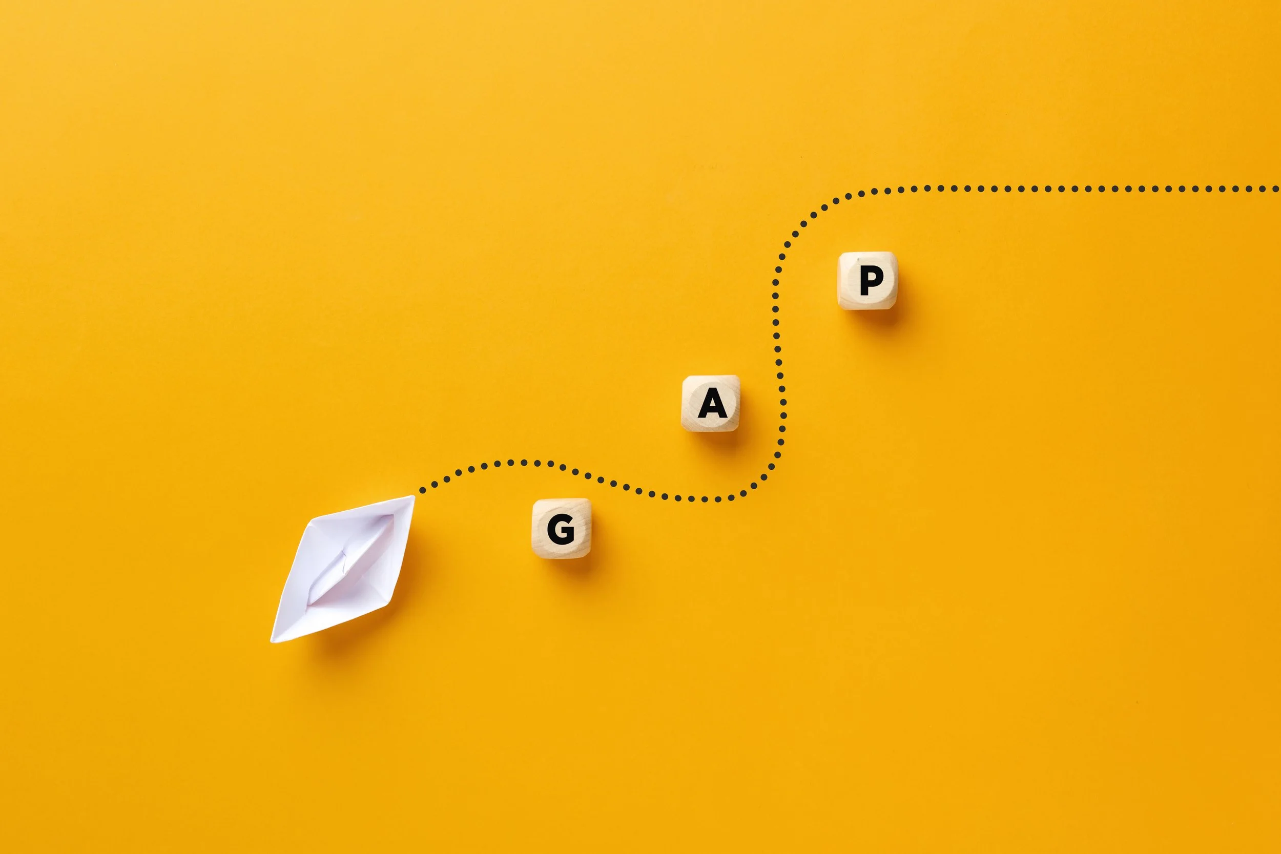 Origami paper boat passes through the wooden cube barriers with the word gap. Gap analysis in business by Gestaldt