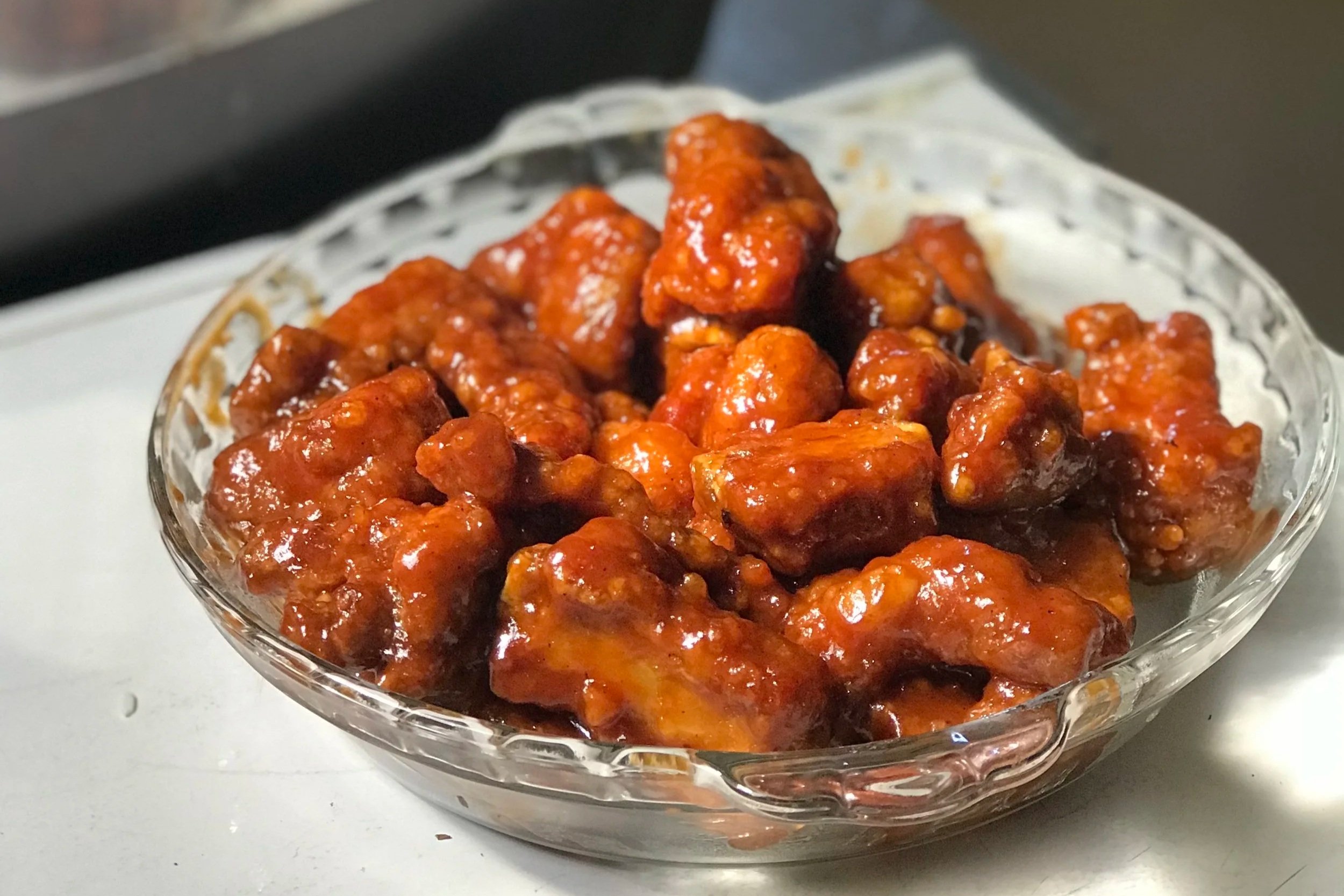 A glass bowl filled with crispy orange chicken morsels covered in a savory, tangy, sweet orange chicken sauce.