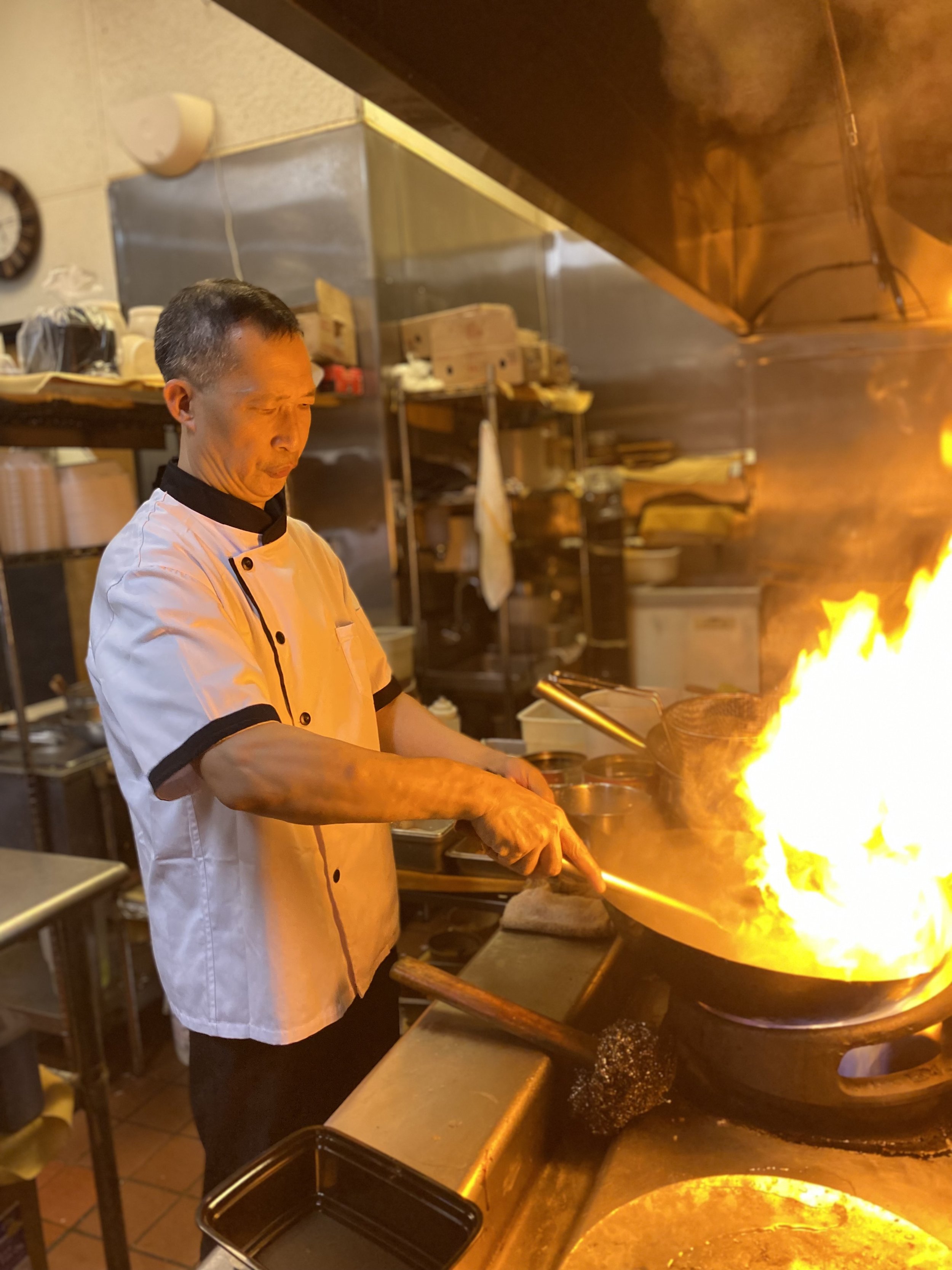 Chef Max Ma in chef attire stir frying in a wok with open flame