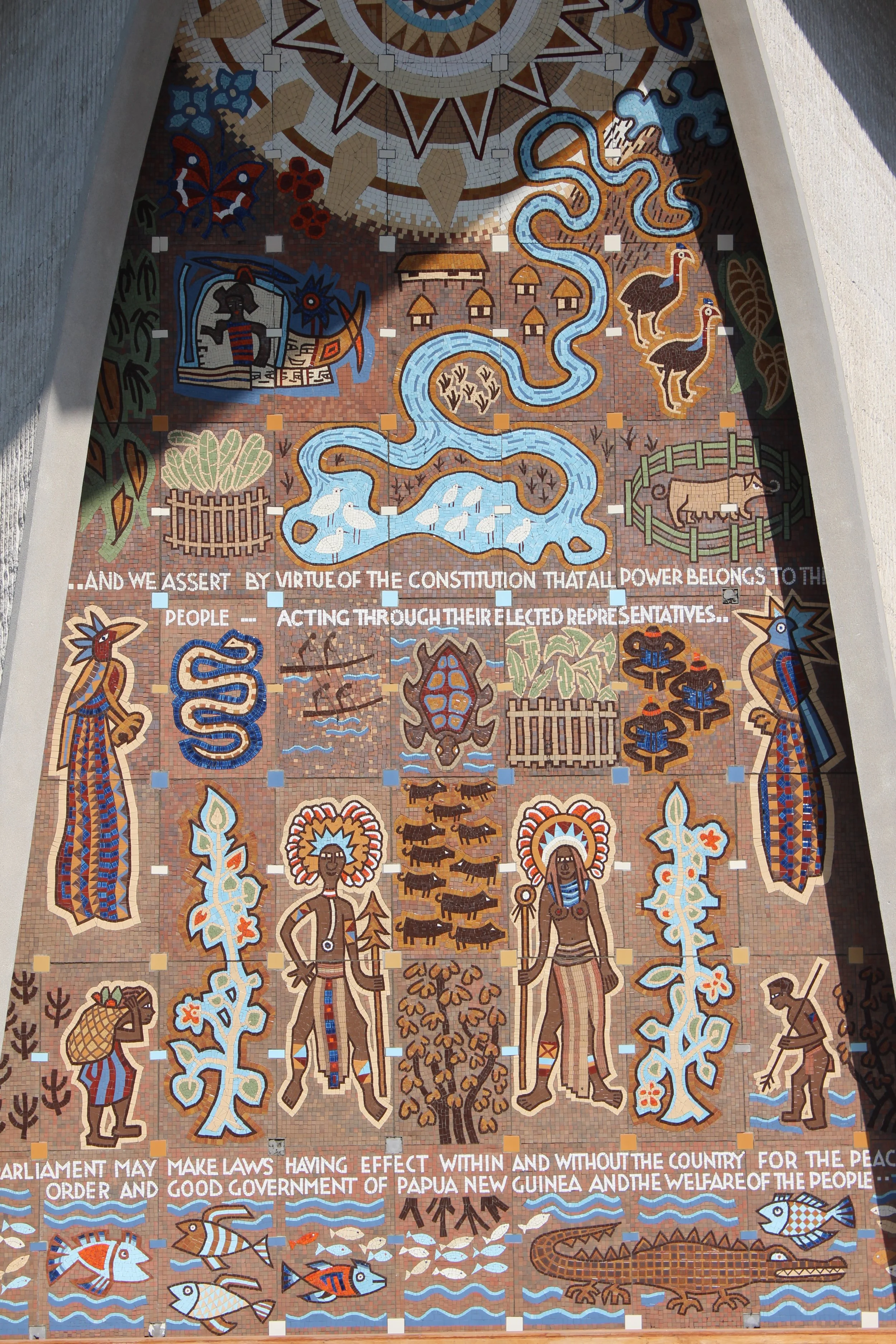 Colorful mural depicting traditional Papua New Guinea art and symbols, including tribal figures, animals, and natural elements, with a quote about the constitution and government.