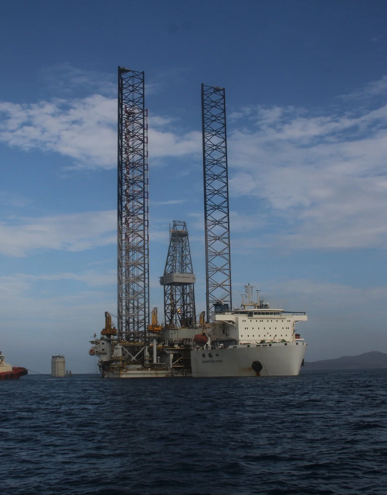 Offshore oil drilling rig in the ocean under a partly cloudy sky.