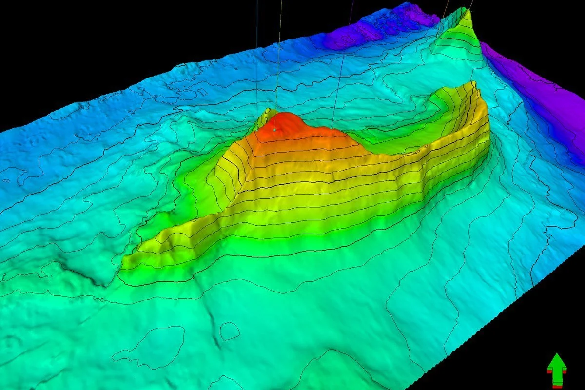 3D topographic map with various elevation contours in vibrant colors, showing a mountainous terrain with peaks and valleys.