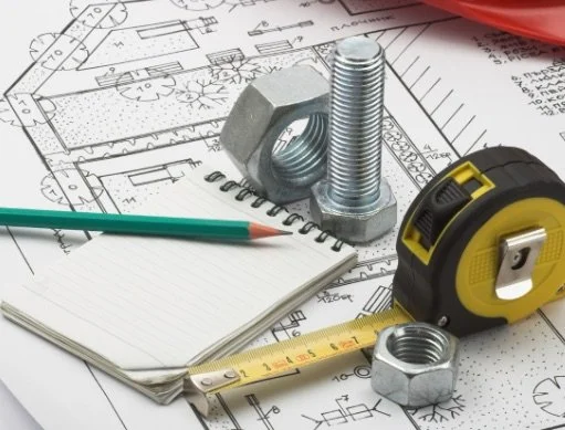 Construction tools and materials on architectural plans, including nuts, bolts, a tape measure, a pencil, and a notepad.