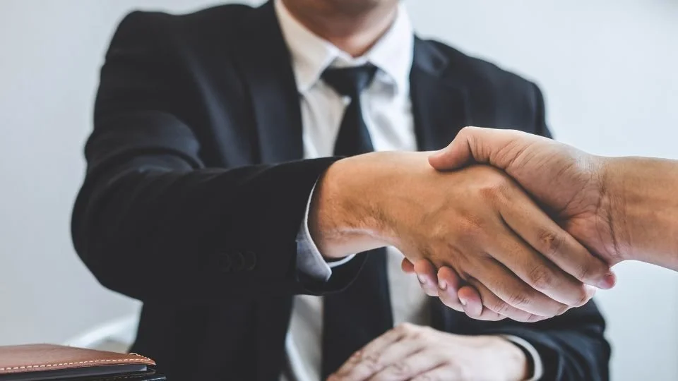 Two individuals in business attire shaking hands in an office setting.