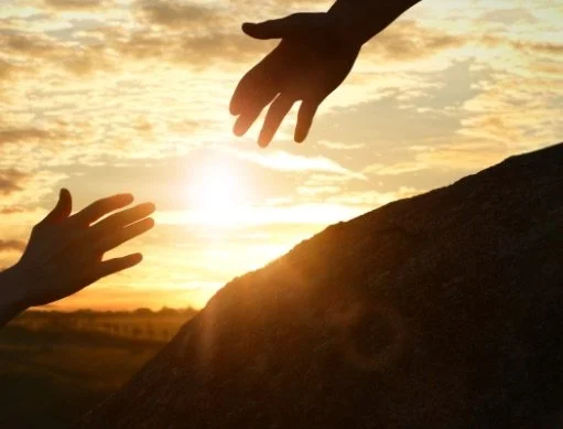 Two hands reaching out to each other at sunset over a hill.