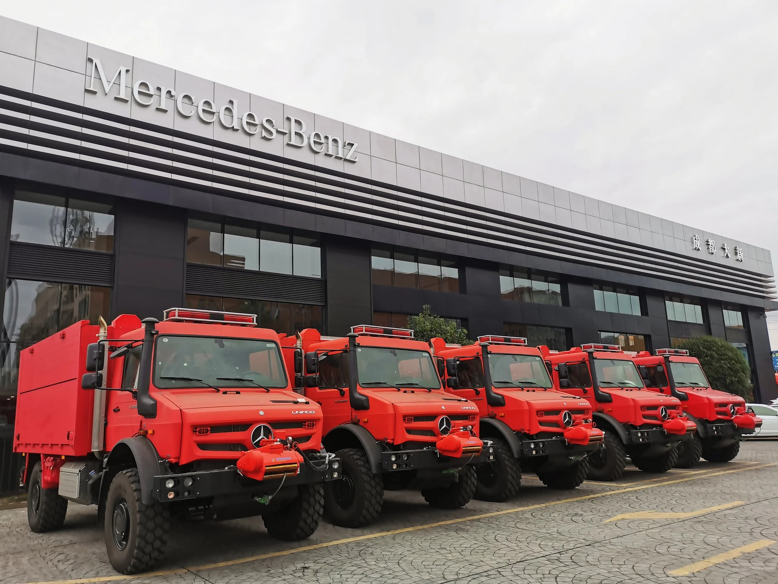 Five red fire trucks parked in front of a Mercedes-Benz building.