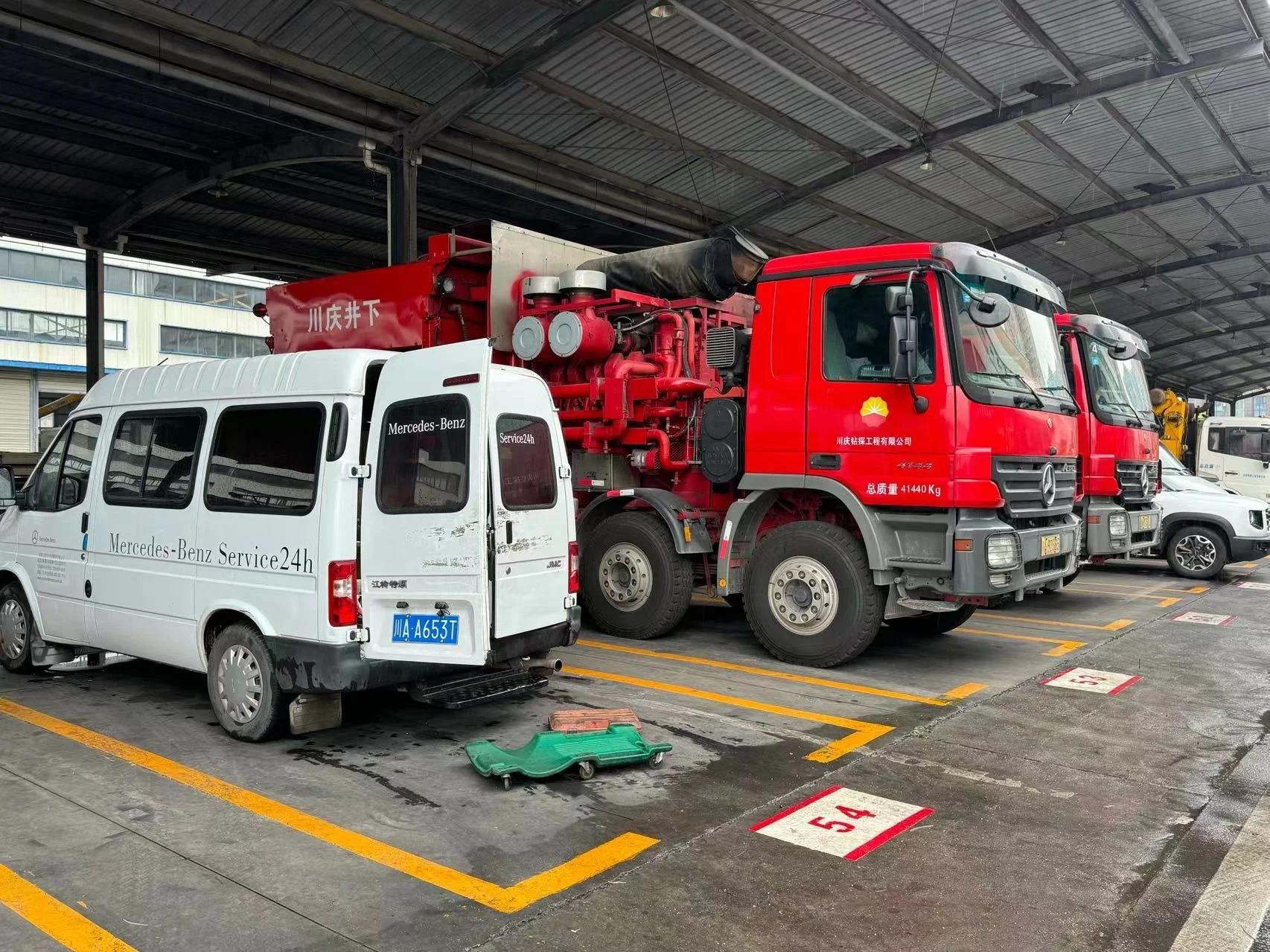 Parking garage with various service vehicles including a white Mercedes-Benz Service24h van and two red fire trucks. The vehicles are parked in marked parking spaces, numbered 54 and 55.