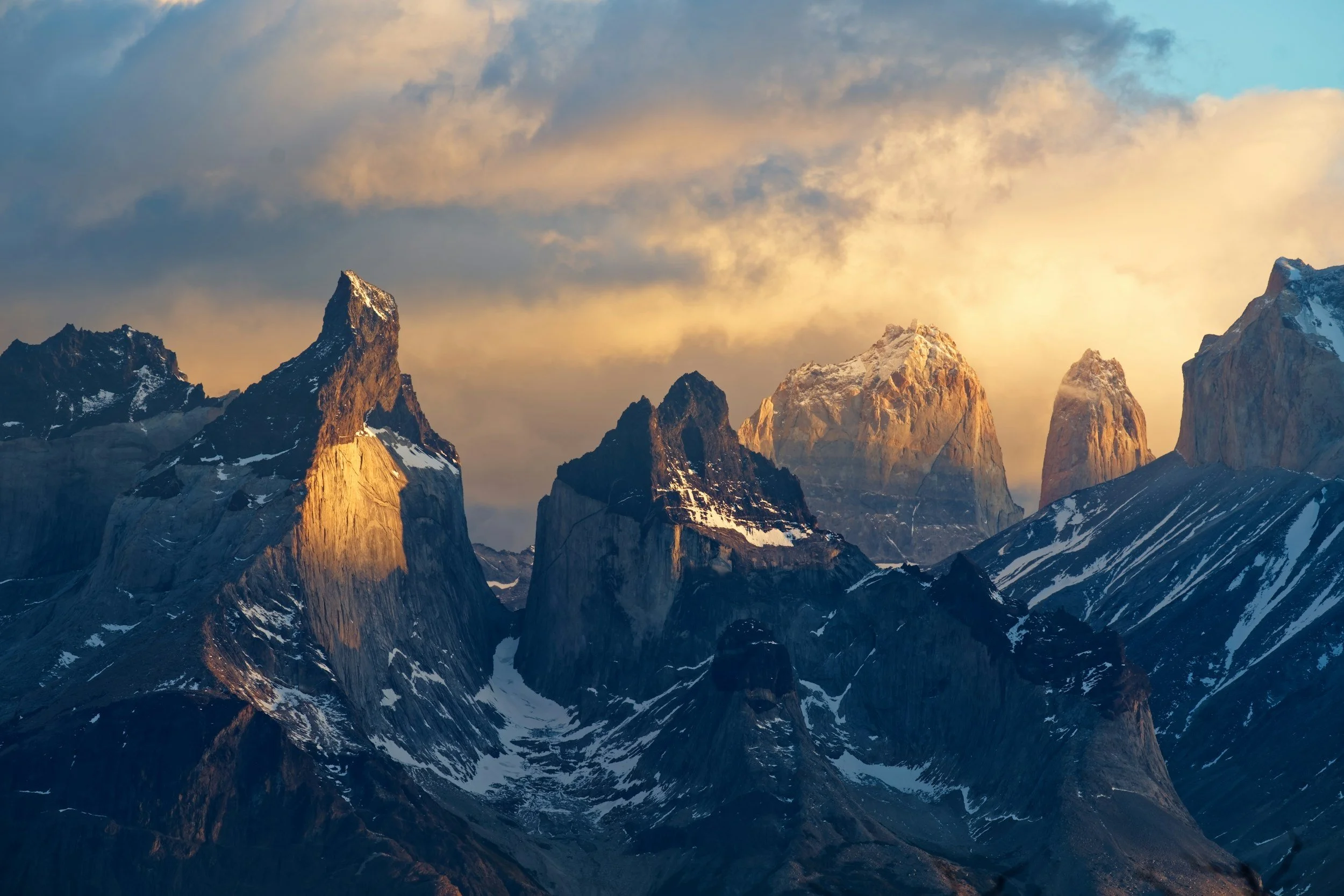 Sunset over rugged mountain peaks with snow patches in a dramatic landscape.
