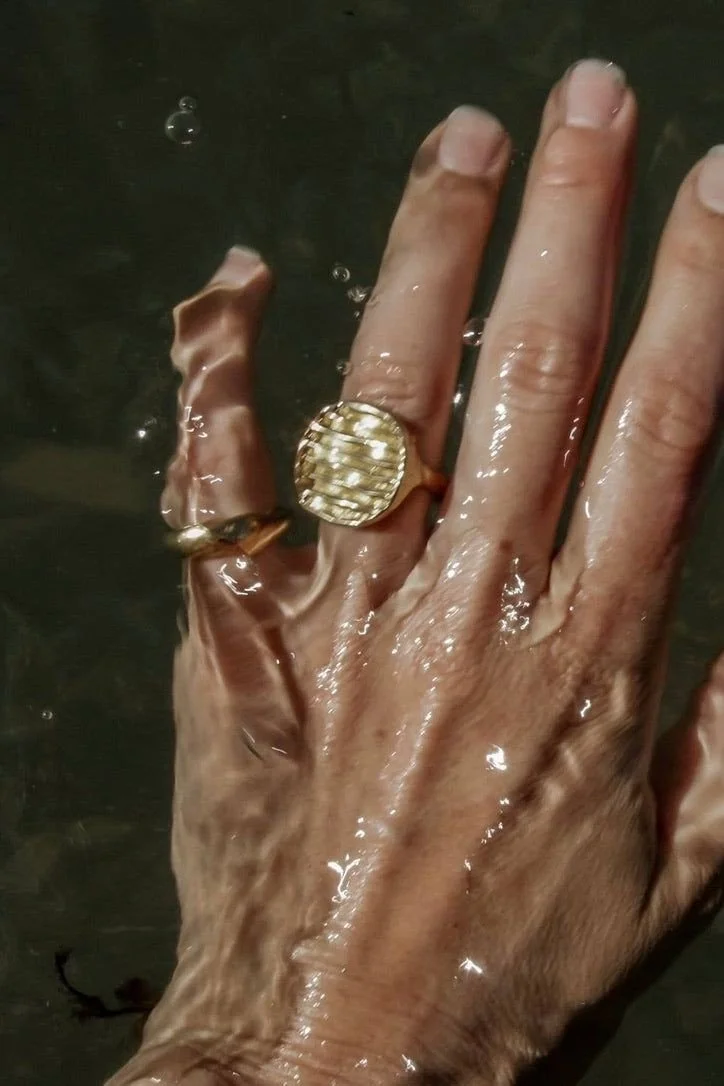 A hand wearing gold rings and a large gold statement ring, submerged in water.