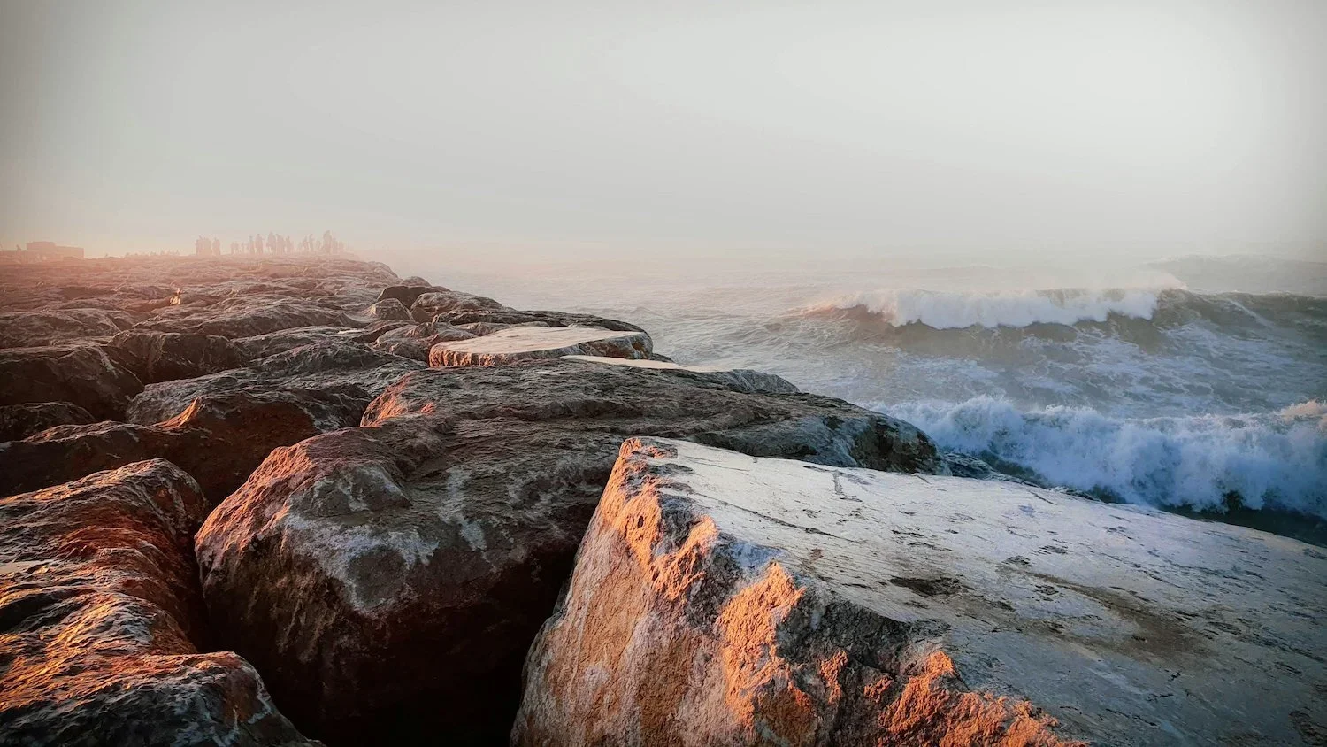 Oceanside rocks with waves crashing and a foggy sky at sunrise