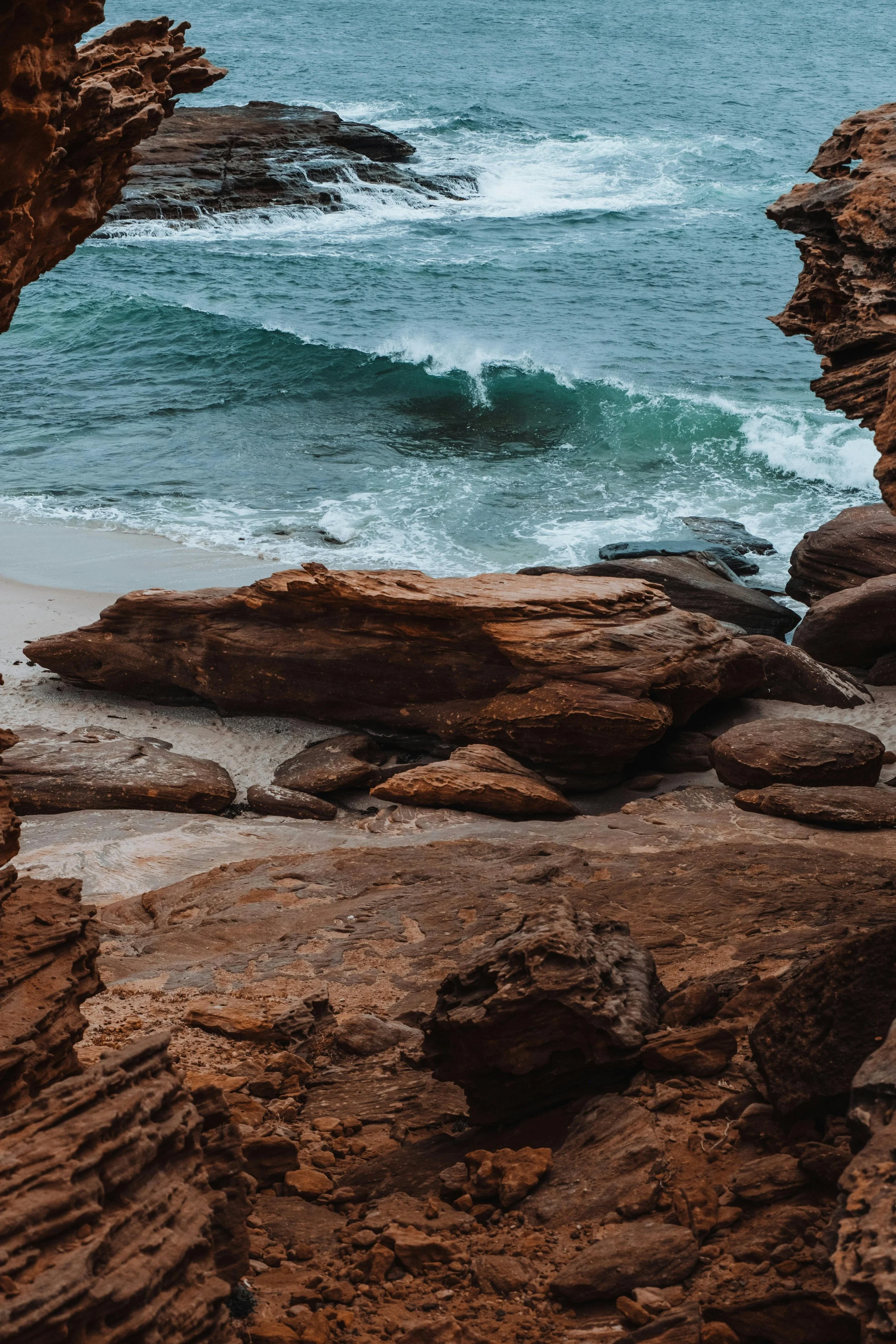 View through a rocky cave opening showing the ocean with waves crashing against rocks on the shoreline.