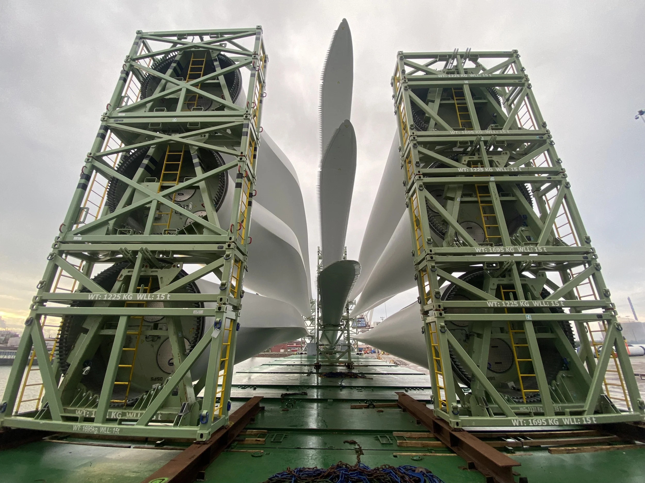 A large wind turbine blade in transport, positioned between two supporting structures on a green platform, for shipment.