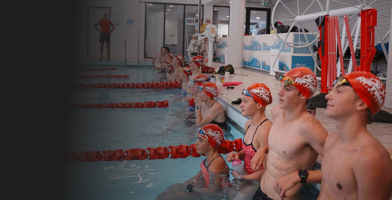 Swimmers in a swimming pool during a swim practice or competition, wearing red swim caps and swim gear, with an instructor or coach nearby.
