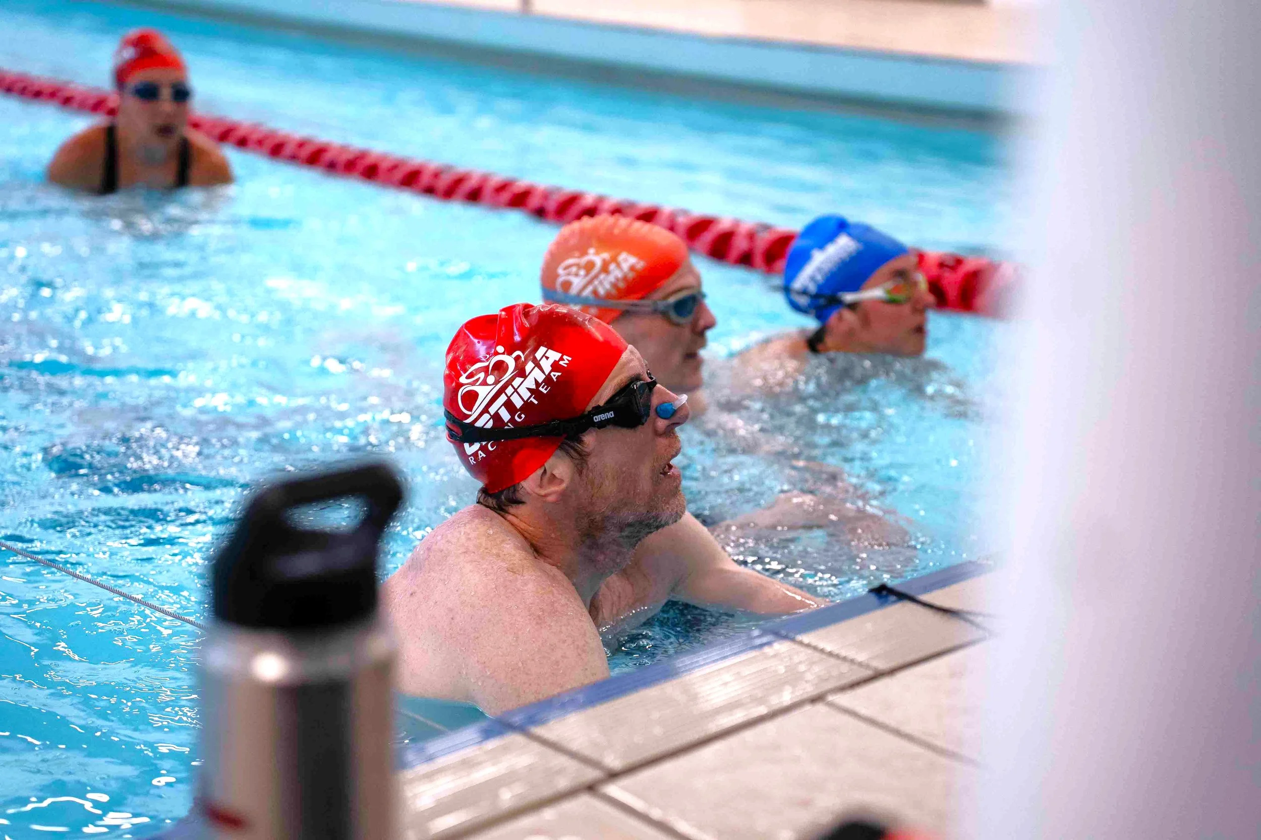 Swimmers in a pool wearing swim caps and goggles during a swimming practice or competition.