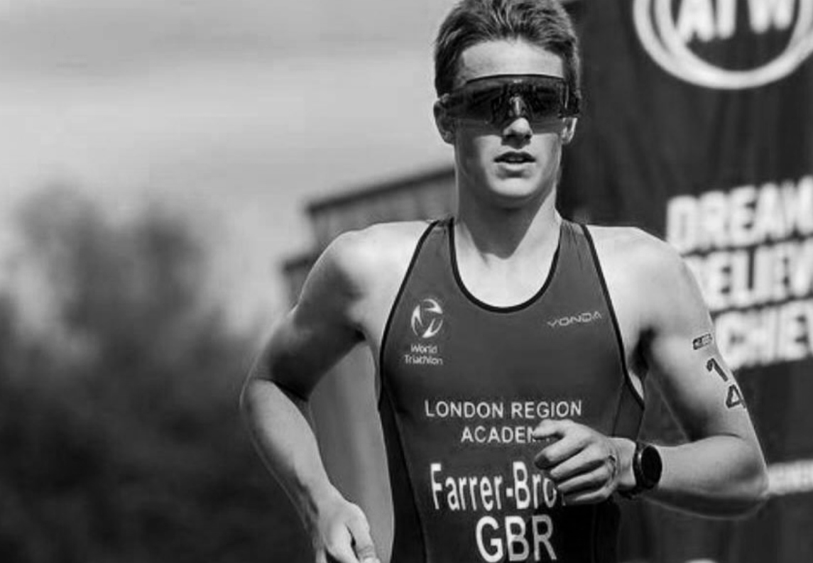 A woman wearing sports sunglasses and a running outfit, participating in a race or triathlon, with a focus on her determined expression and athletic posture.