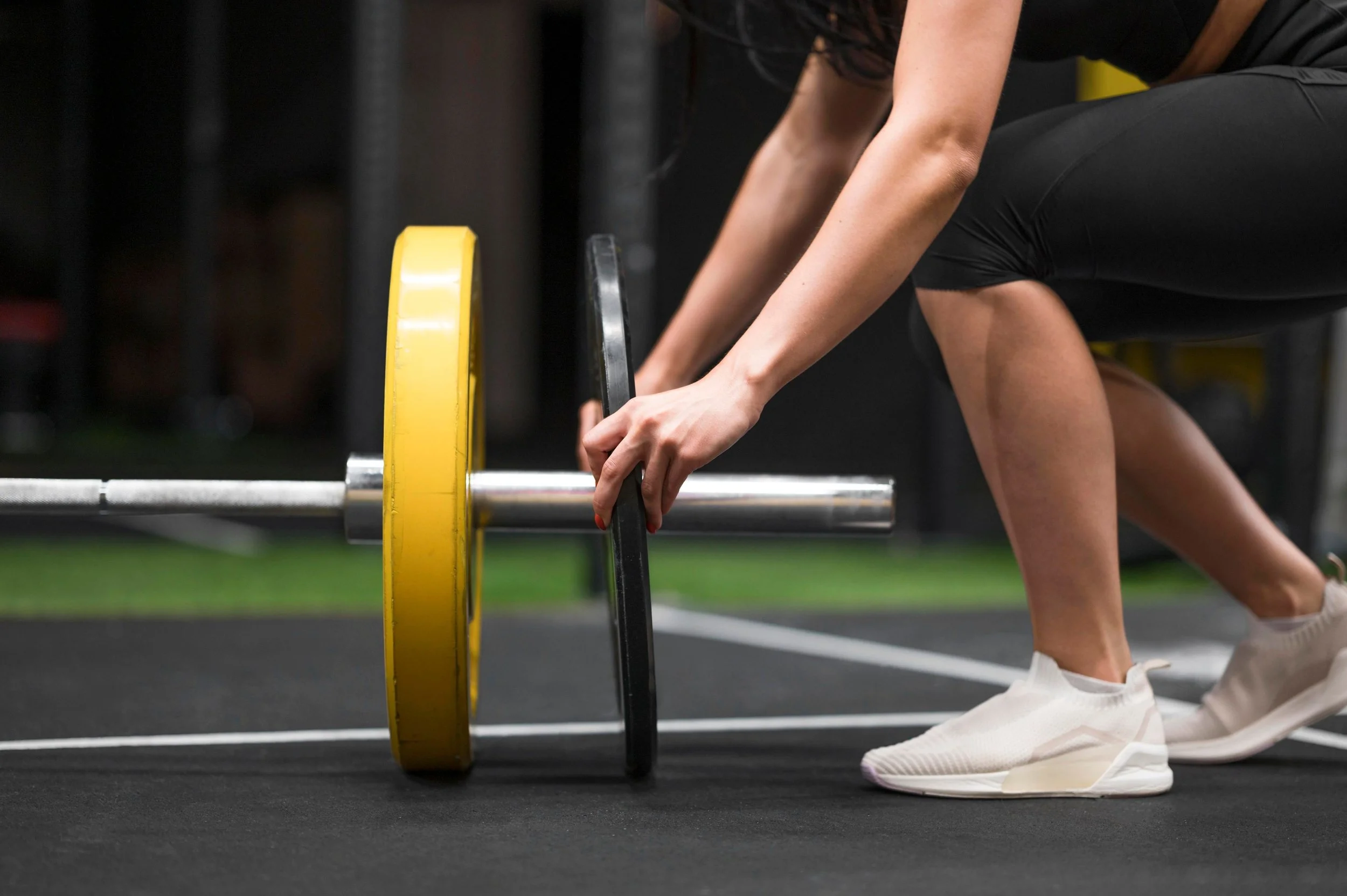 A woman prepares to lift a barbell loaded with yellow and black weights in a gym.