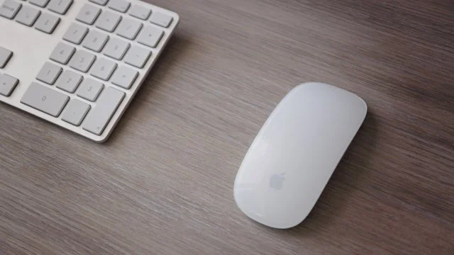 Keyboard and Apple Magic Mouse on a wooden desk.