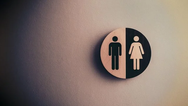 A circular sign indicating a men's and women's restroom, with the men's figure in black on the left and the women's figure in black on the right.