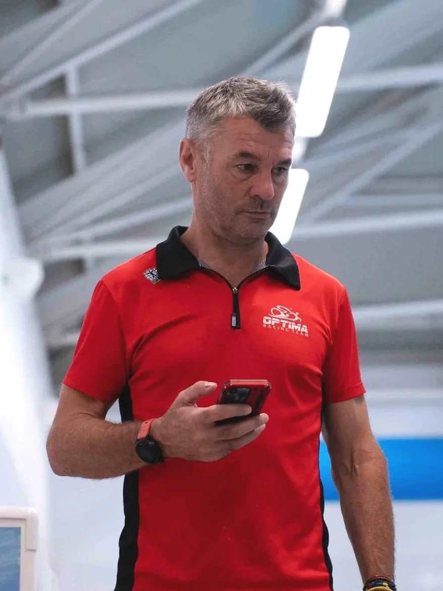 A man in a red and black shirt looking at his phone indoors under bright ceiling lights.