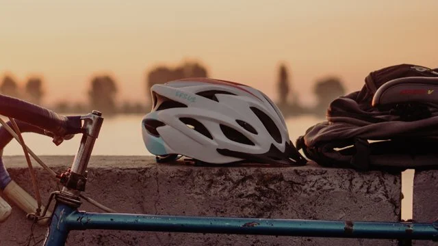 A bicycle with a helmet and backpack resting on a stone ledge during sunset.