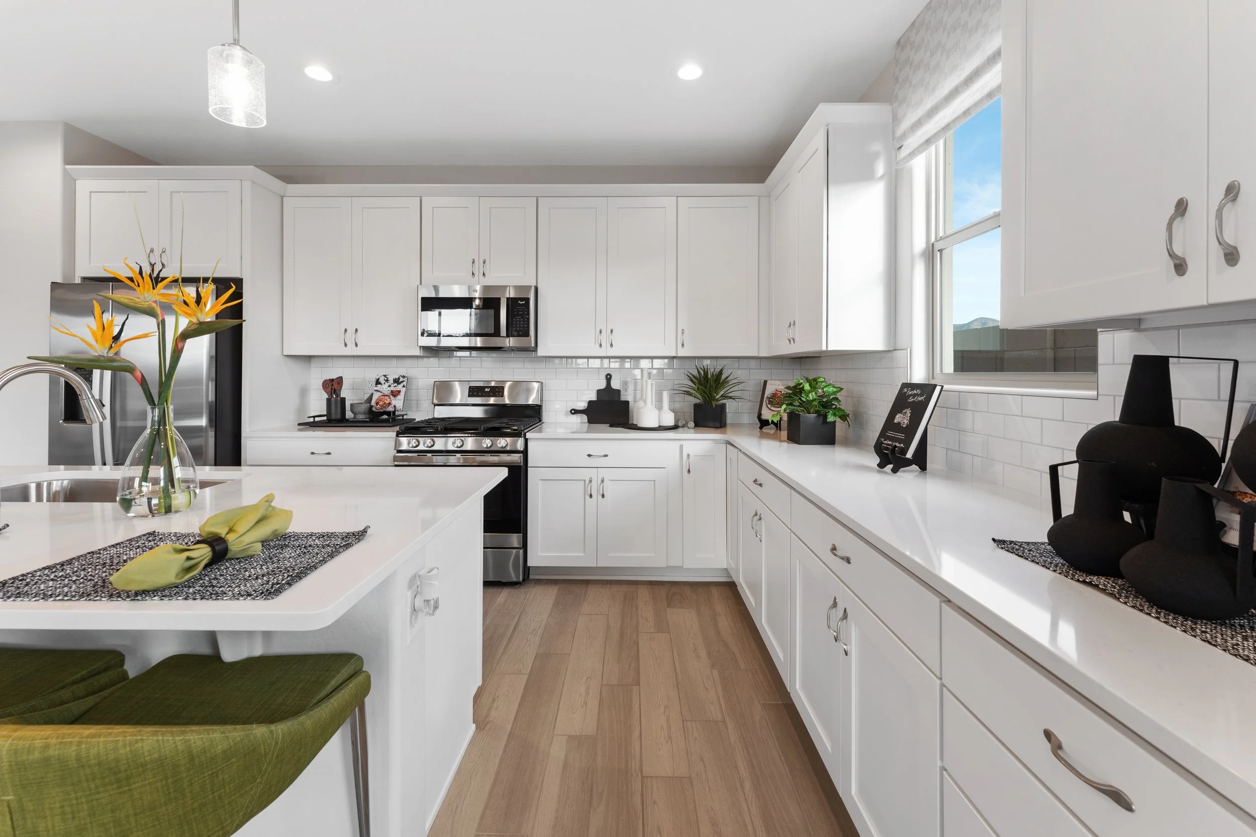 Modern kitchen with white cabinets, stainless steel appliances, and a wooden floor, decorated with plants and kitchenware.