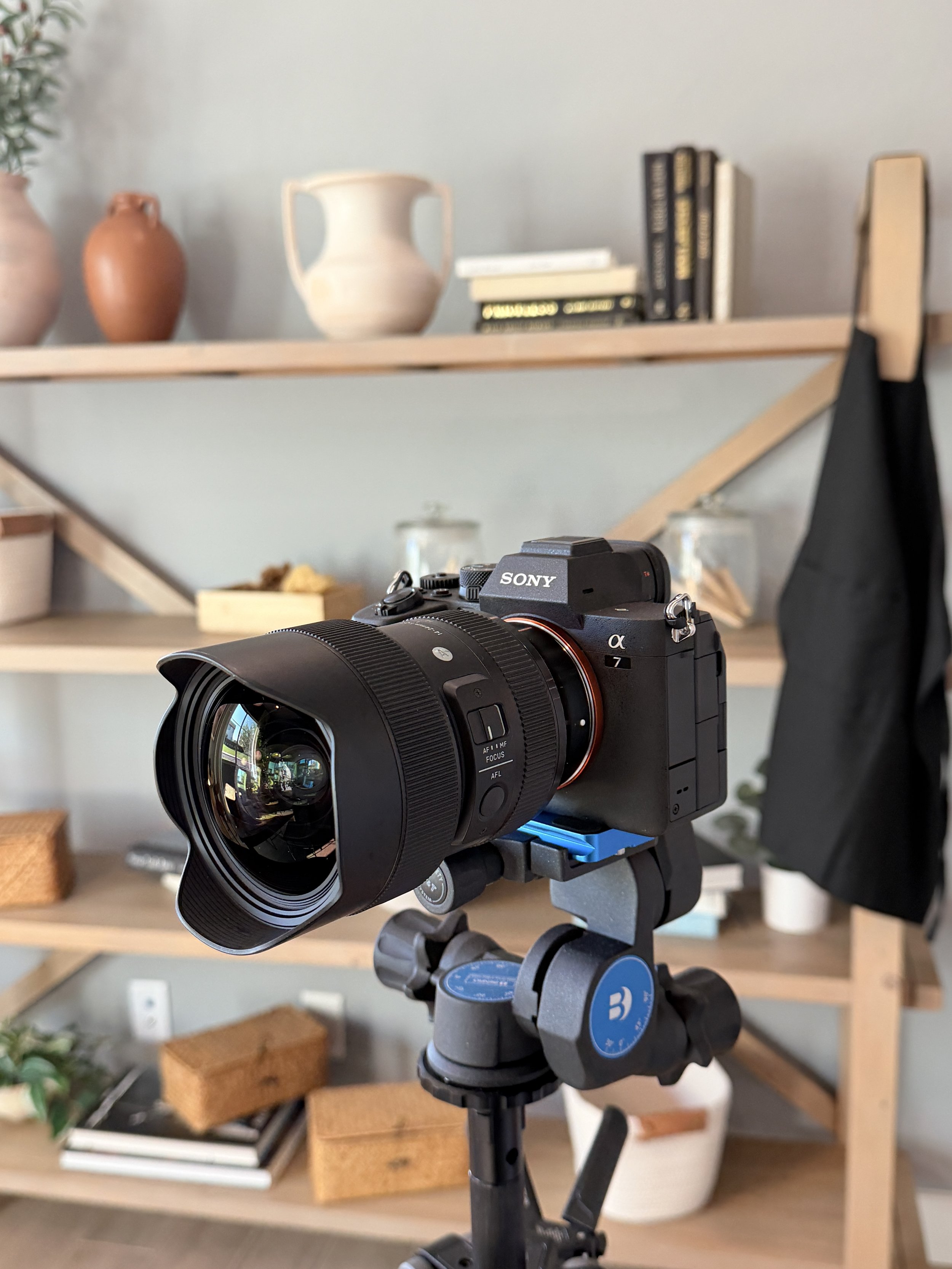 Camera on tripod focused inward, set in a room with wooden shelves containing various vases, books, and decorative items.