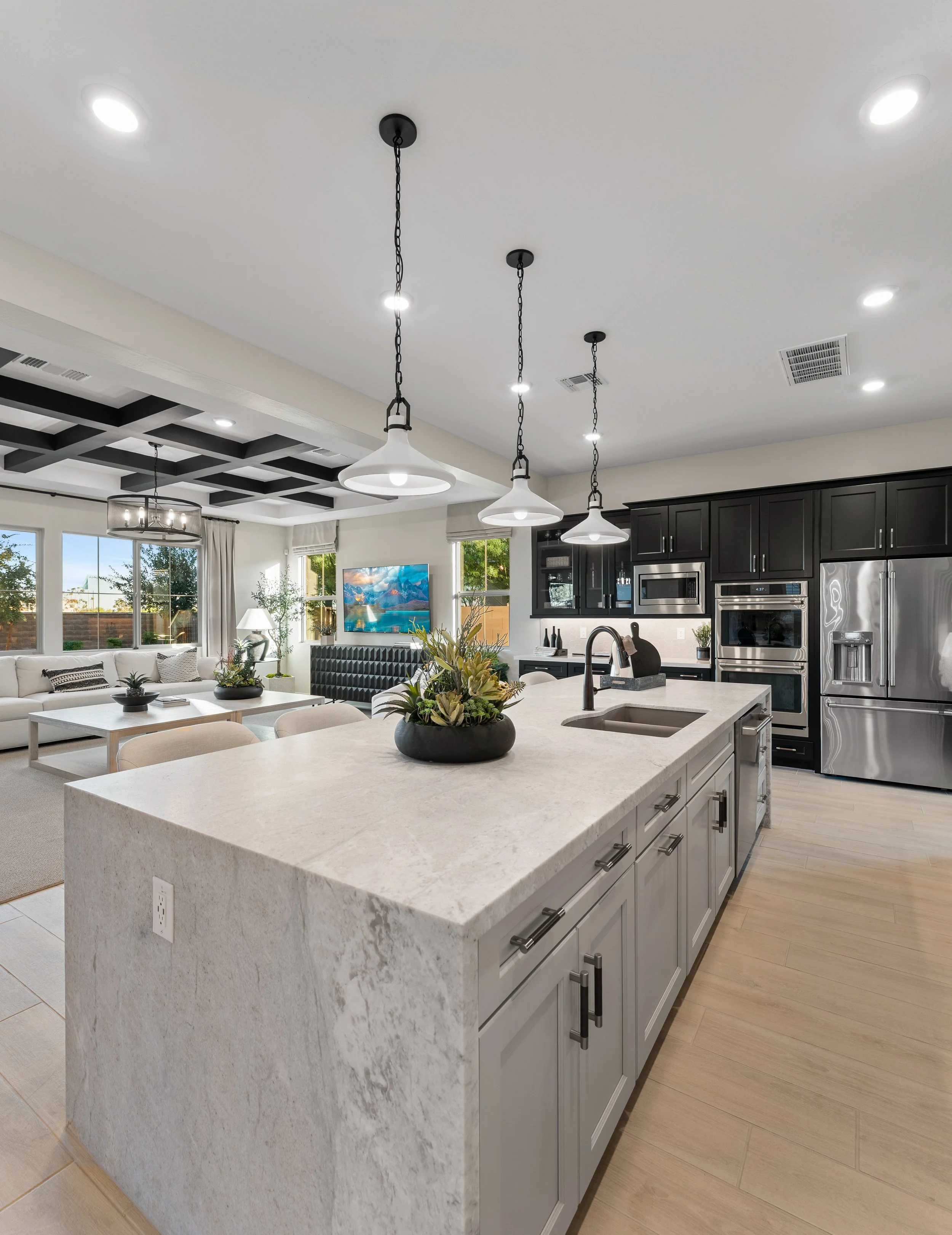 Modern open-concept kitchen and living room with white marble kitchen island, black cabinets, stainless steel appliances, and a cozy sitting area with a TV.