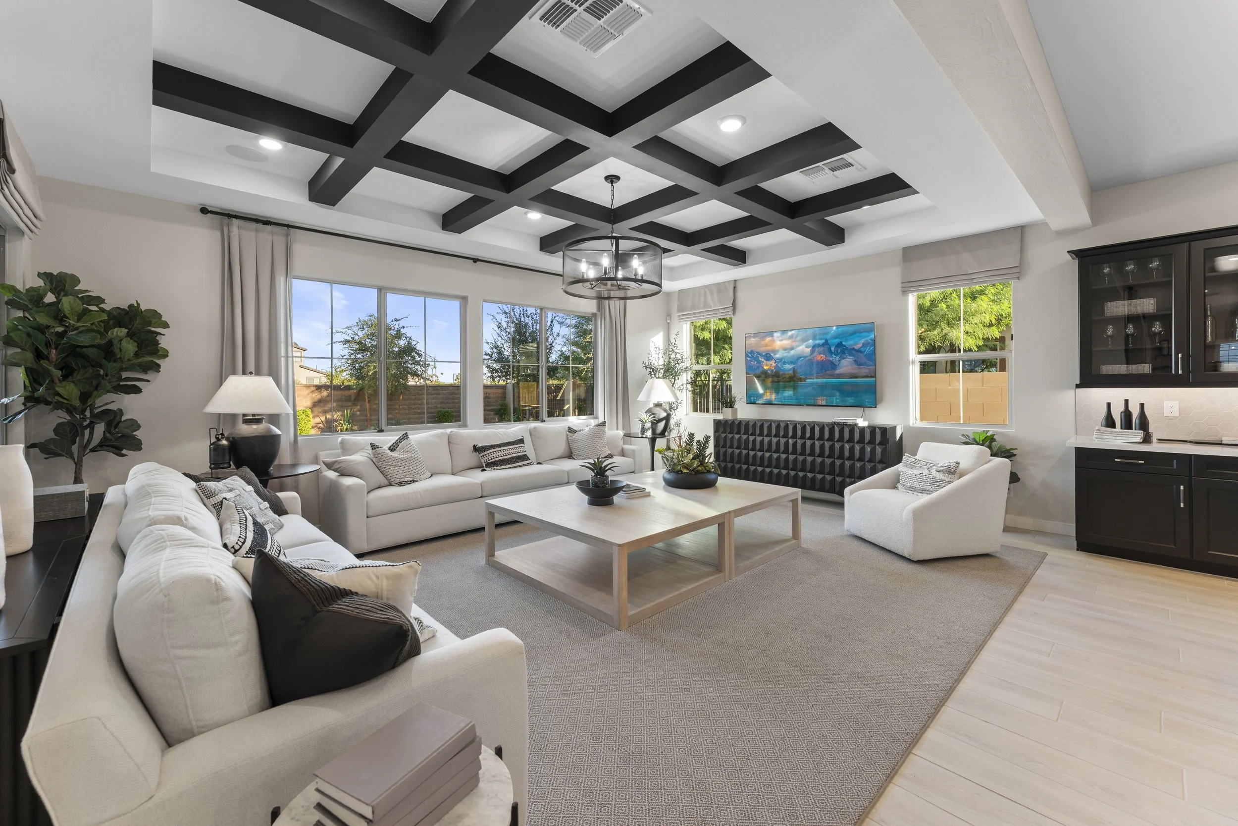 Spacious living room with white sofas, black and white pillows, large windows, wooden coffee table, black cabinet, mounted flat-screen TV, and minimal decor.