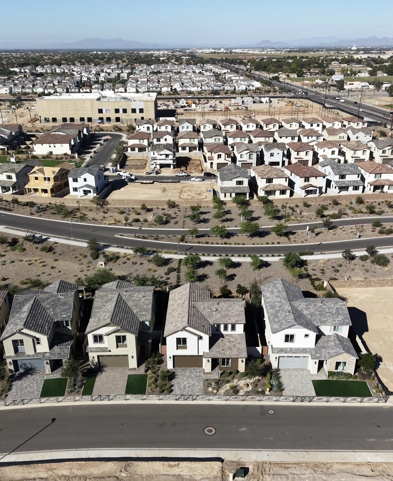 Aerial view of a suburban neighborhood with newly built houses, some under construction, surrounded by roads, trees, and open land.